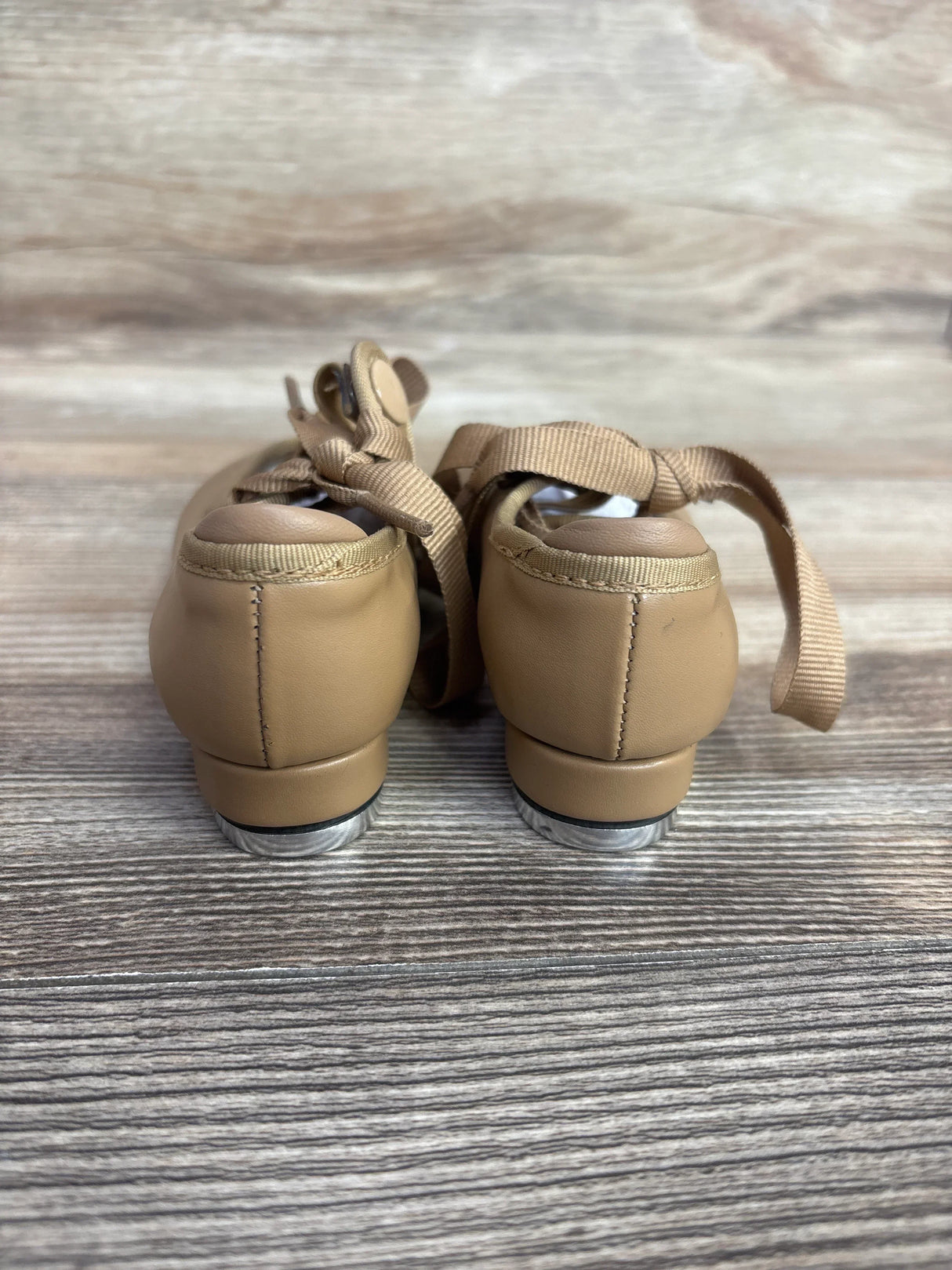 Rear view of tan toddler tap dance shoes with ribbons on wood background