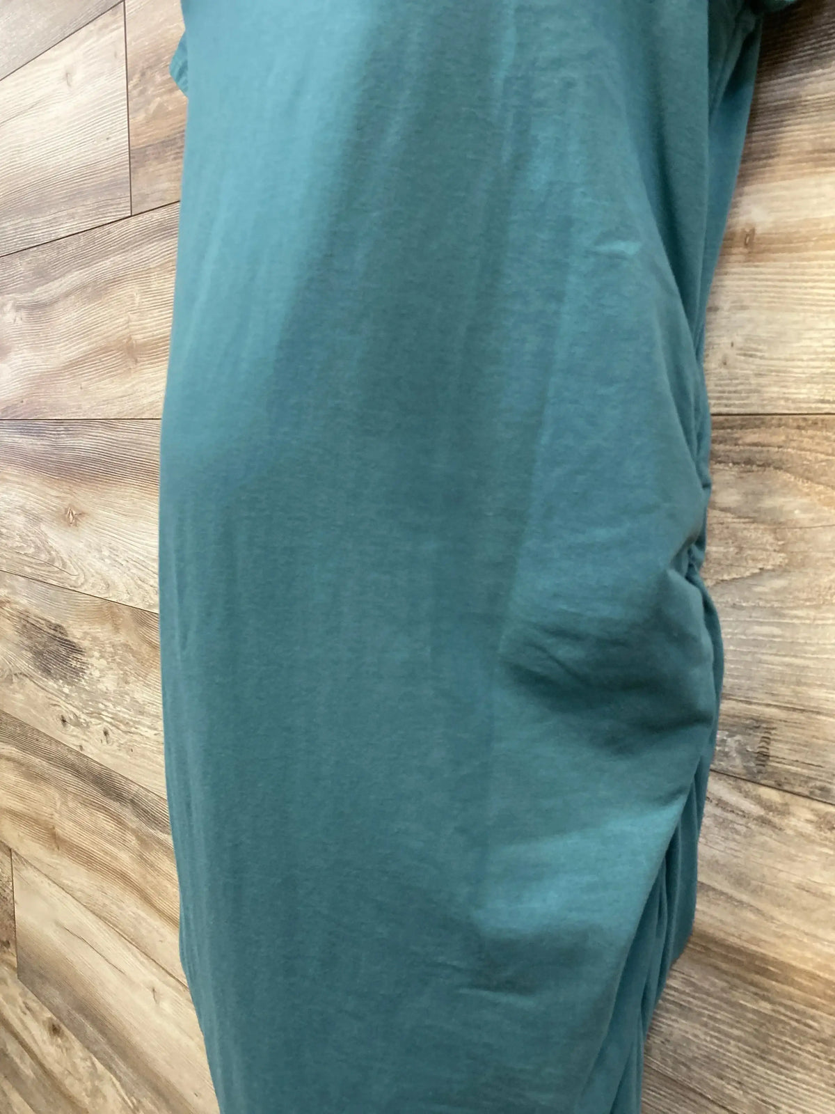 Side view of green Isabel maternity bodycon dress (XL) showing ruched side seam and fitted silhouette on wood plank background