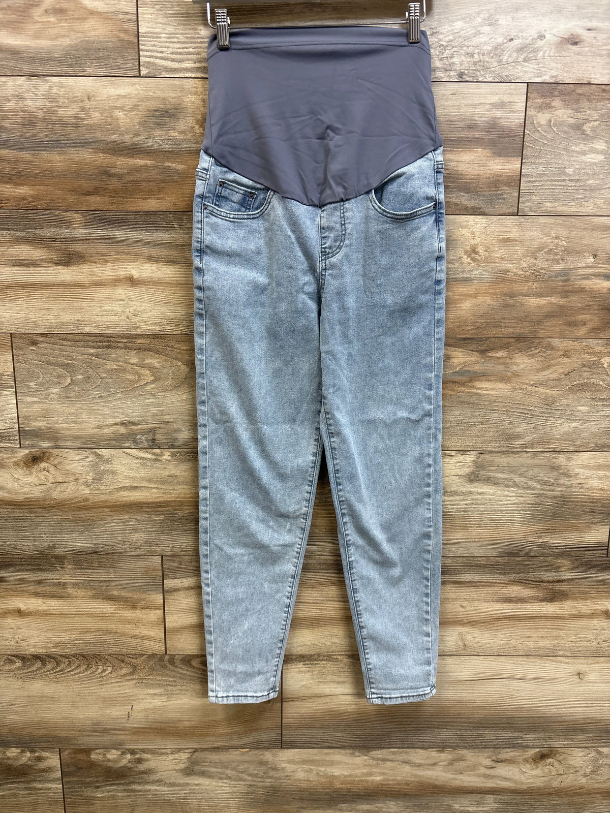 Flat-lay view of blue maternity jeans in size Small showcasing a gray over-belly panel and front pockets on a wood floor