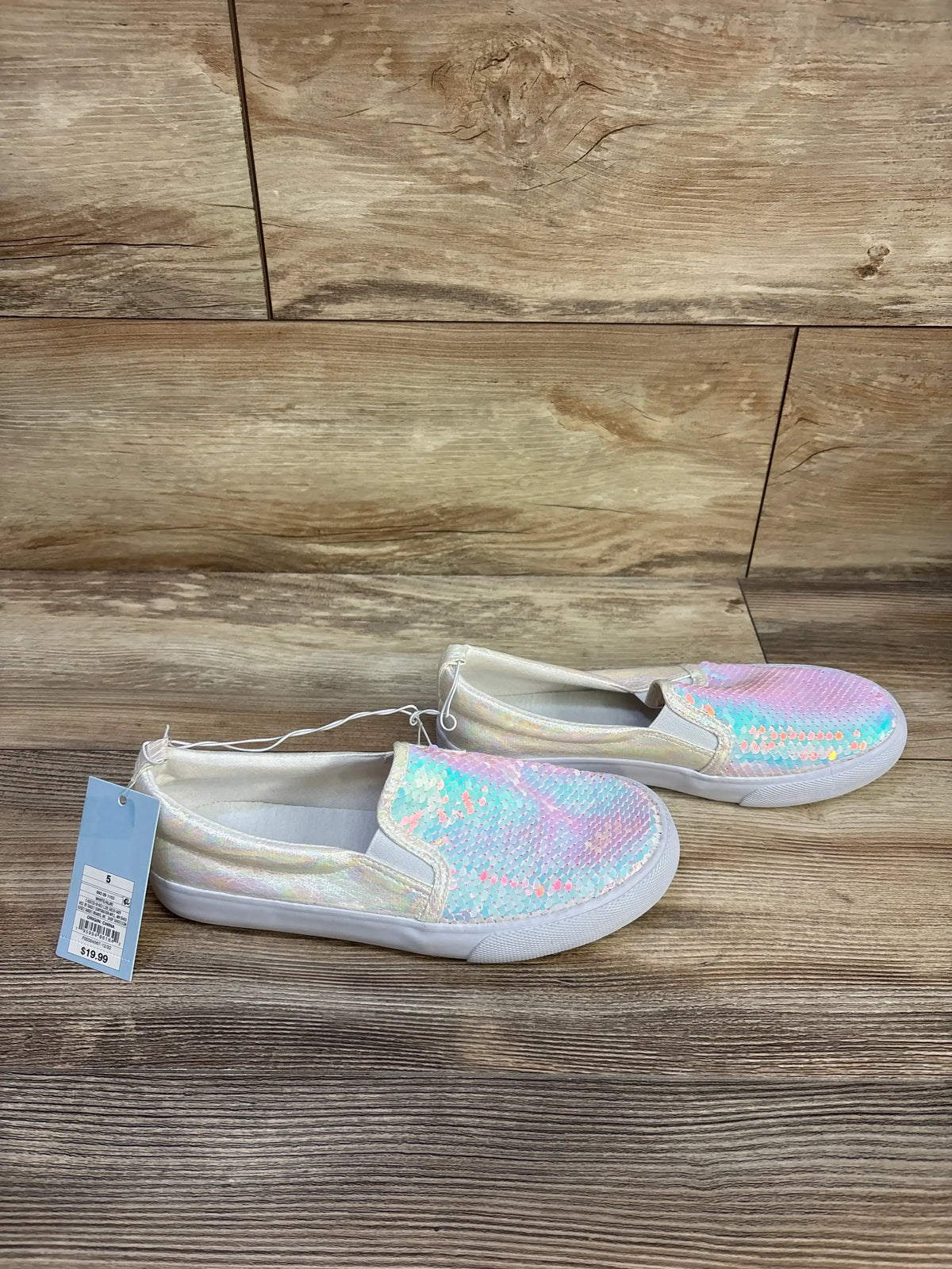 Side view of Cat and Jack Aliki sneakers showcasing iridescent pastel sequin upper and white sole on wood background, size 5Y on tag