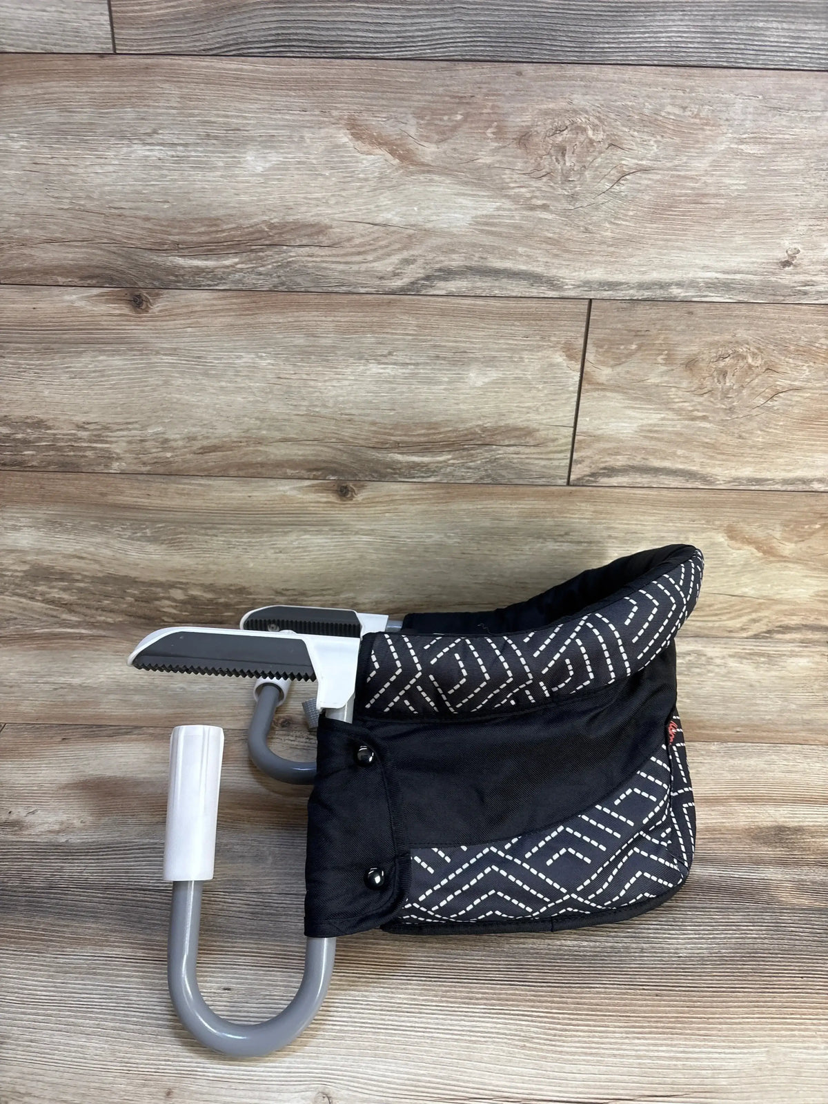 Front view of MTWML Hook On High Chair - Black Stripe showcasing black geometric seat fabric, gray clamp arms, and safety straps on a wooden floor