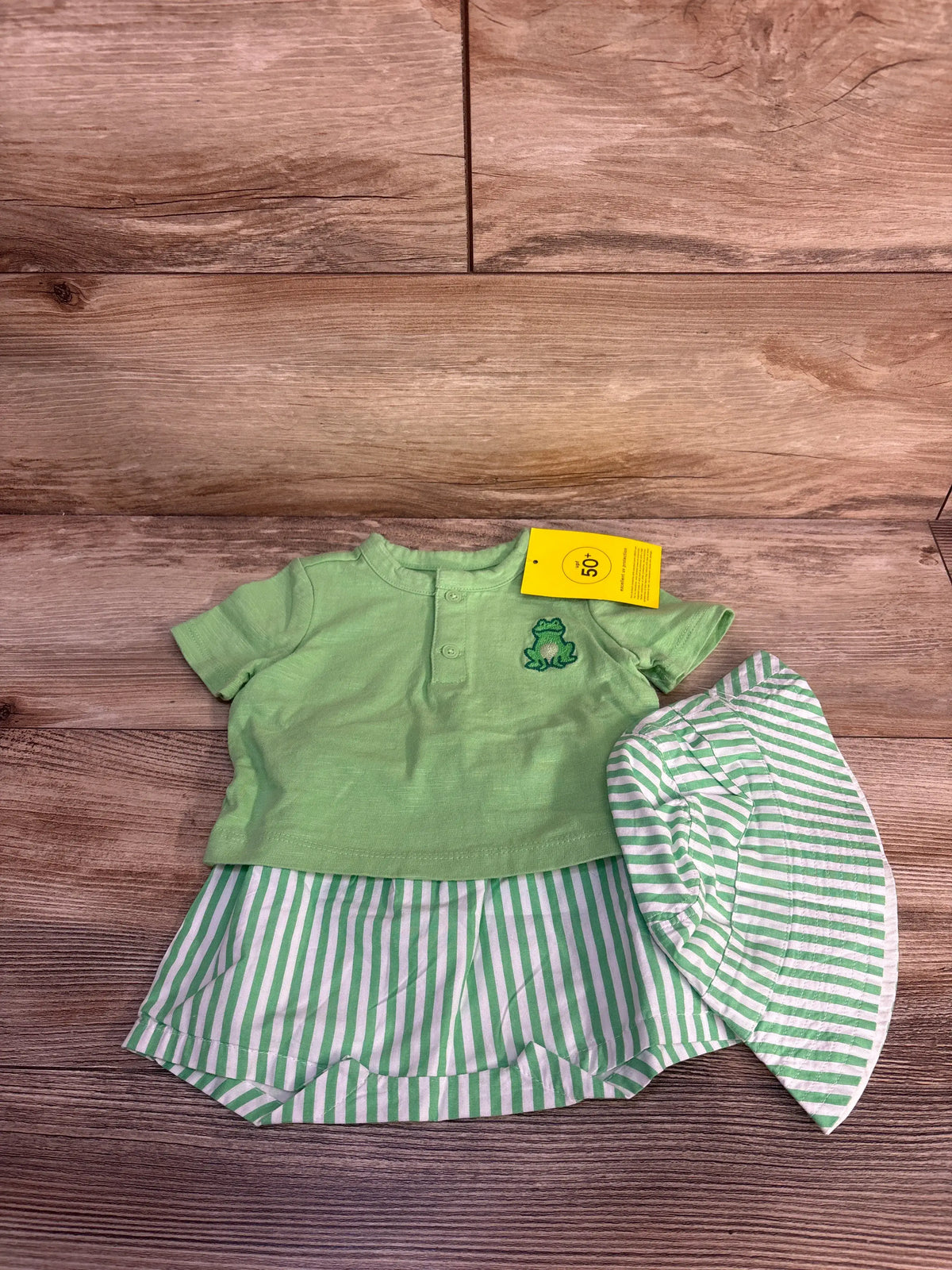 Front view of green Baby Gap frog outfit set with frog embroidery, striped shorts, and matching bucket hat on wood