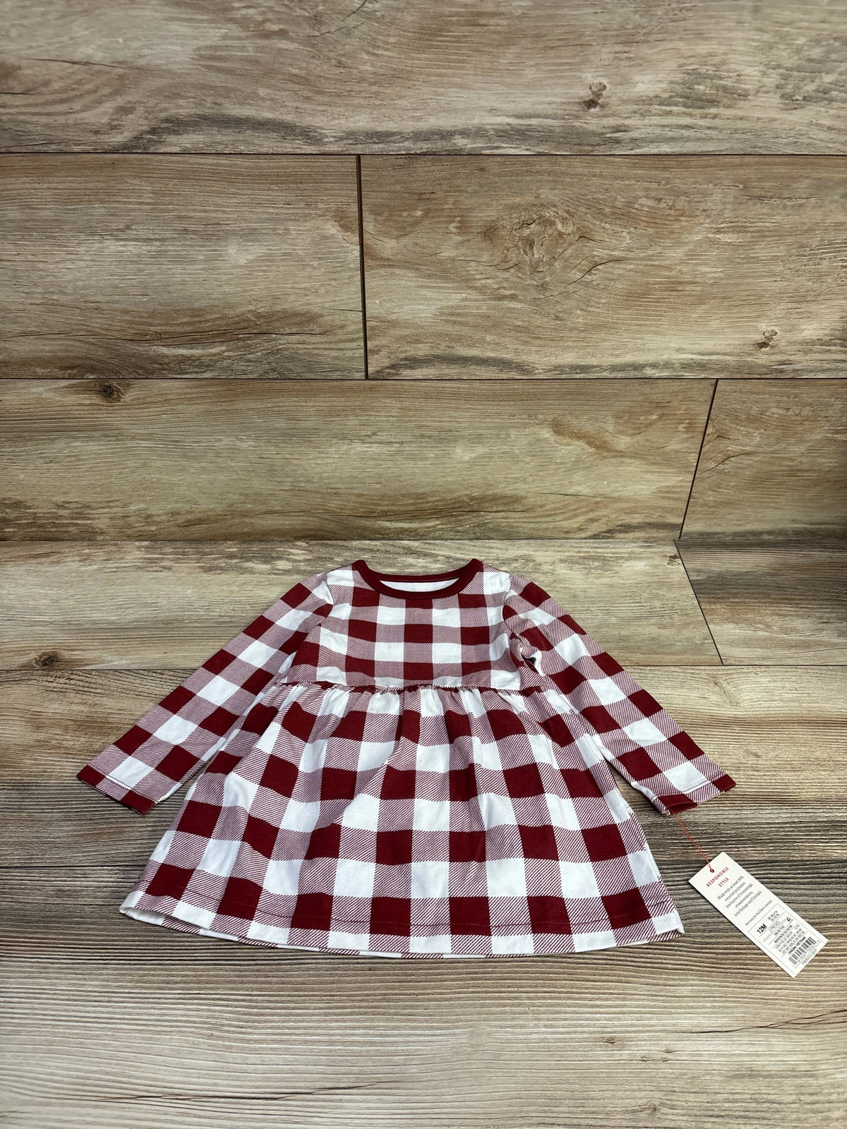 Top view of a red and white gingham long-sleeve baby dress with a gathered waist on a wood-grain background