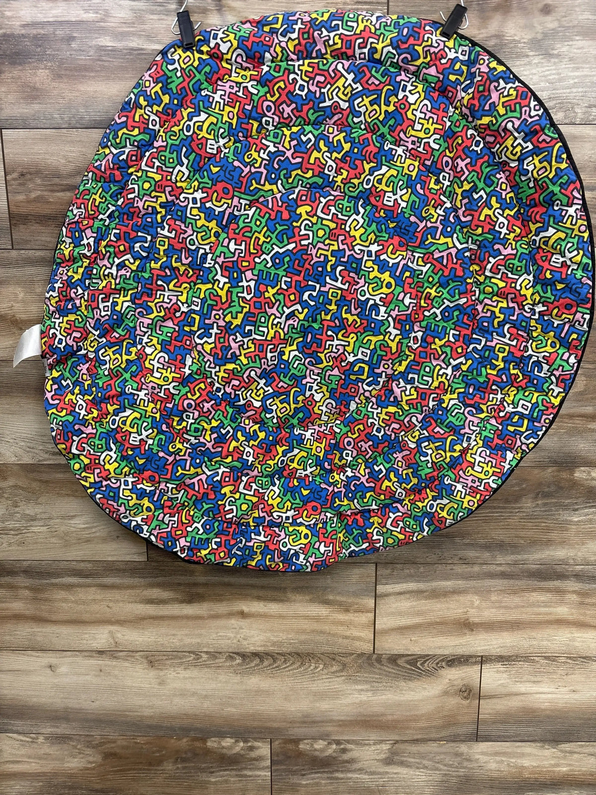 Overhead view of Etta Loves x Keith Haring reversible playmat showing multicolored print and black edge on wood floor