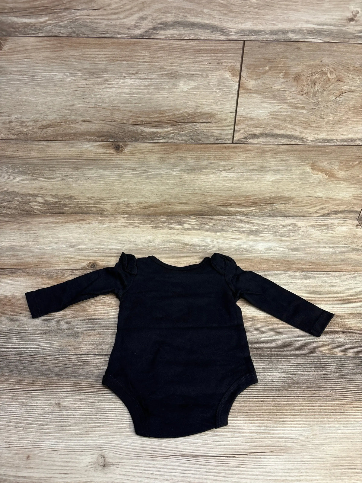 Black long-sleeve baby onesie with ruffled shoulder details on wooden floor