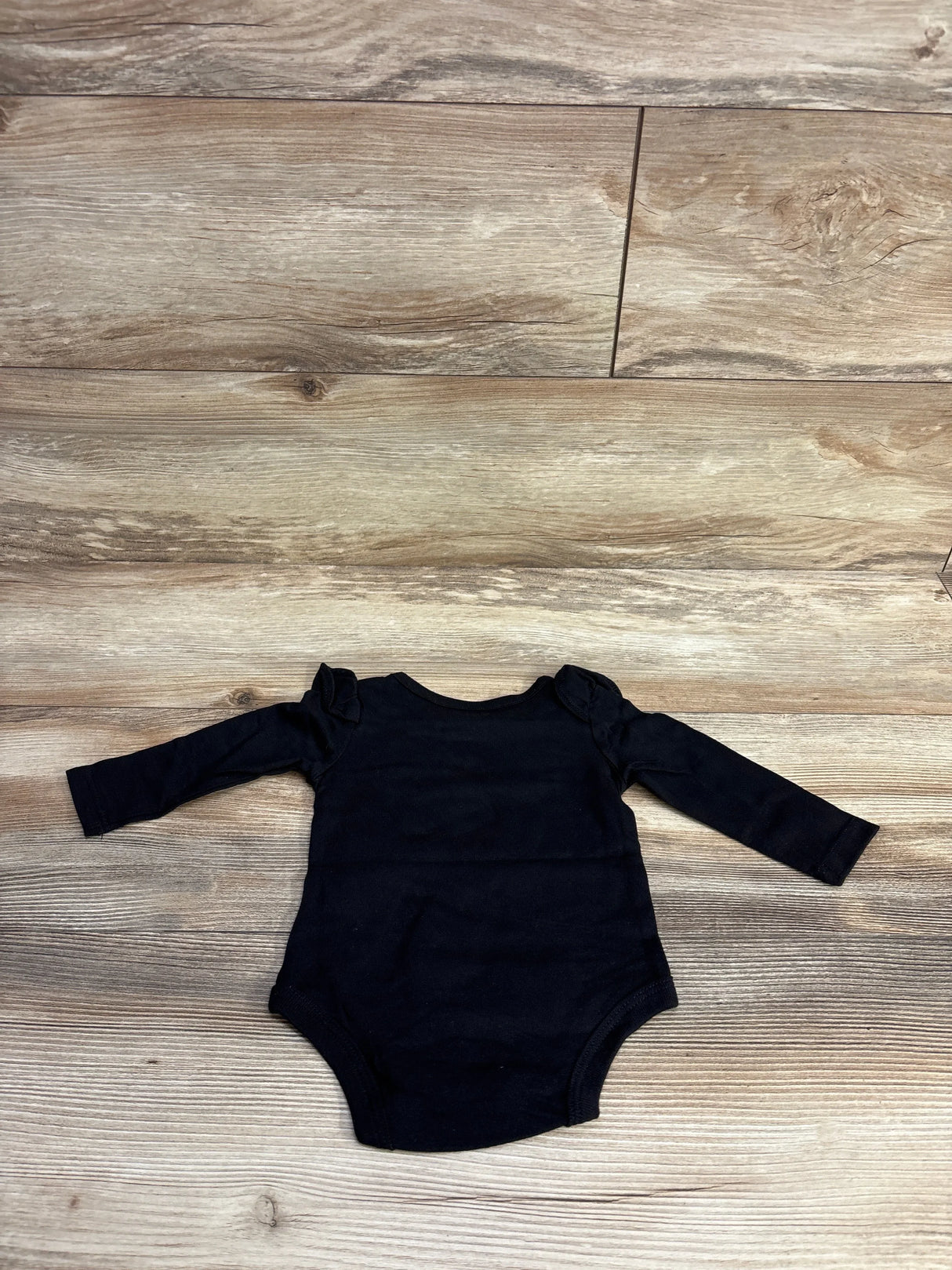 Black long-sleeve baby onesie with ruffled shoulder details on wooden floor