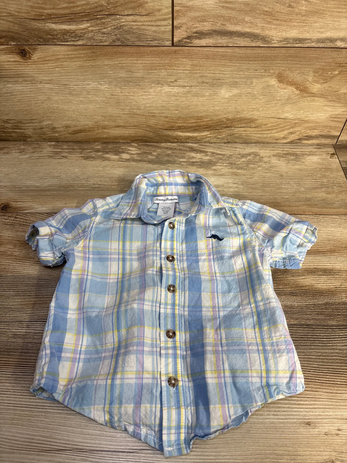 Front view of Tommy Bahama blue button-up shirt in size 4T showcasing plaid pattern and short sleeves on a wood-grain background