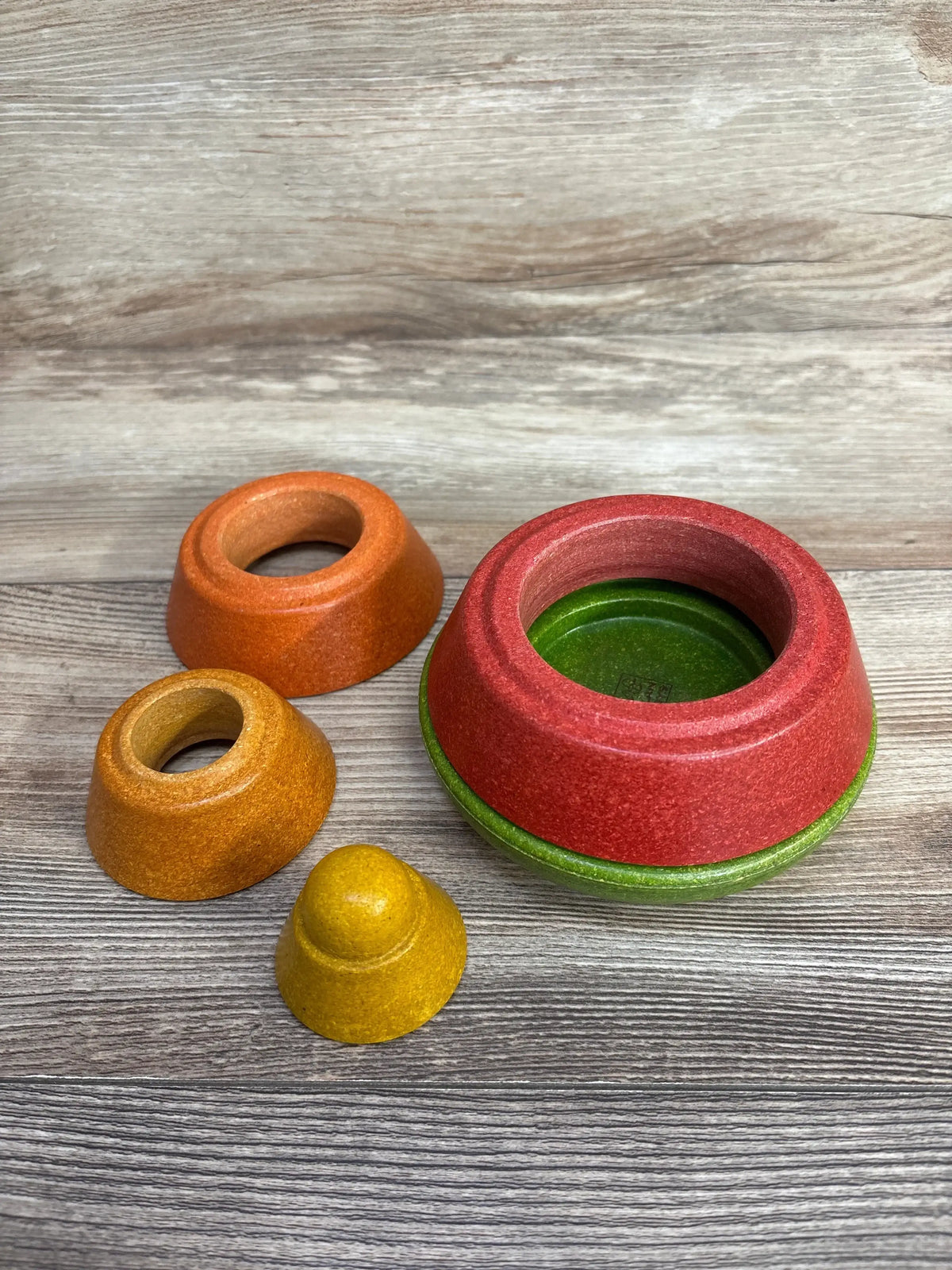 Angled view of Plantoys Cone Stacking Toy showing four colorful stackable wooden cones red, green, orange and yellow on a light wood surface