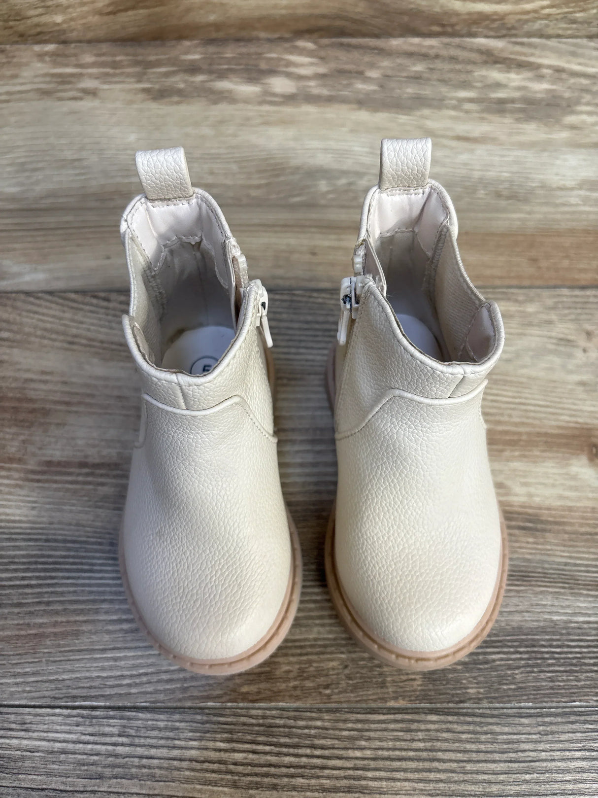 Top-down view of Cat & Jack Chelsea boots size 5C showing cream faux-leather upper, side zippers, and pull tabs on a wood floor