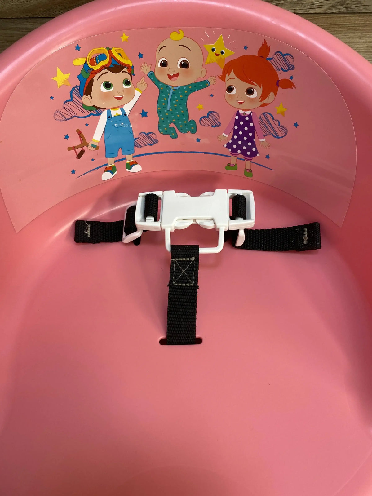 Top view of Cocomelon 15-inch children’s seat showing back character graphic and black safety harness on wood floor