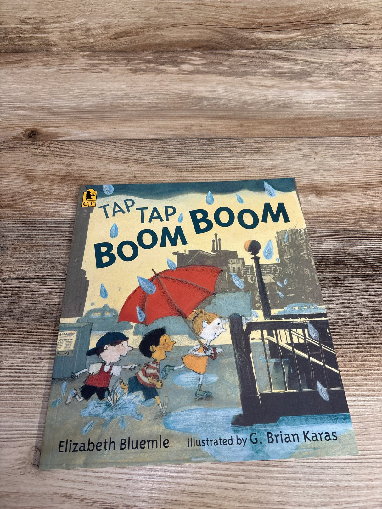Children running in rain with red umbrella on cover of Tap Tap Boom Boom book by Elizabeth Bluemle