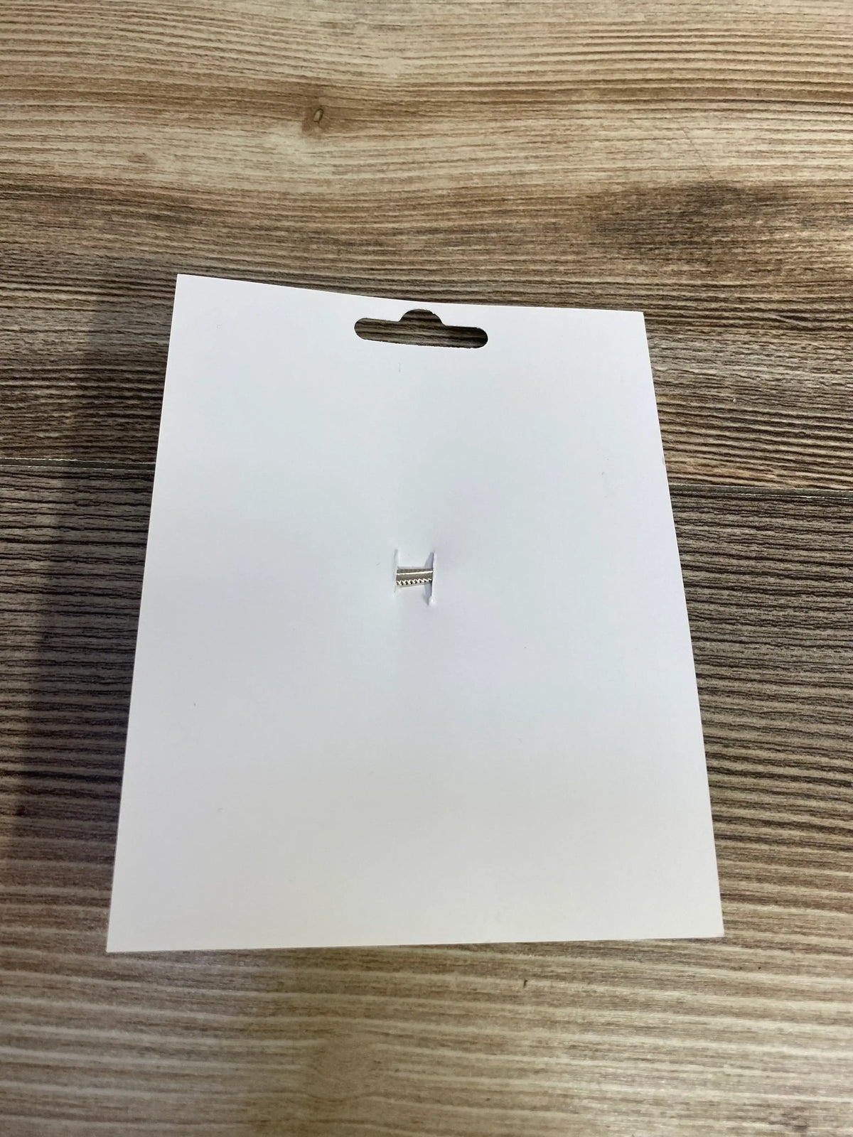 Silver H-shaped earring on white card against wood background