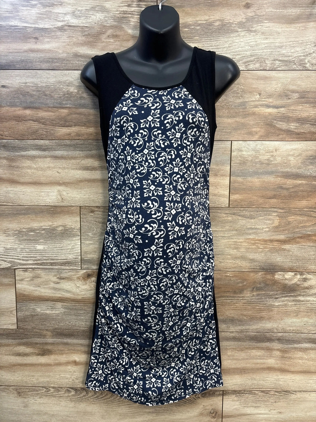 Front view of Kimi and Kai tank maternity dress in black with white floral print and ruched belly against wood backdrop