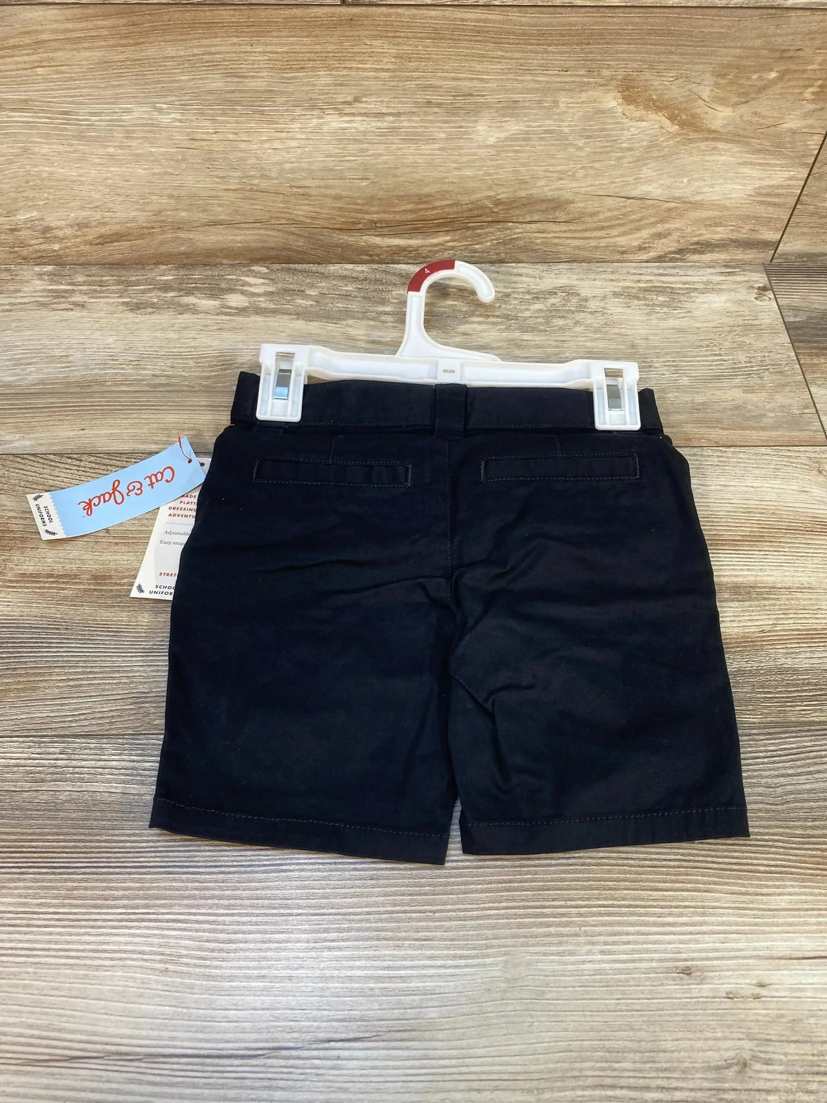 Back view of Cat & Jack black toddler school uniform shorts showing rear welt pockets on a plastic hanger with wood floor background