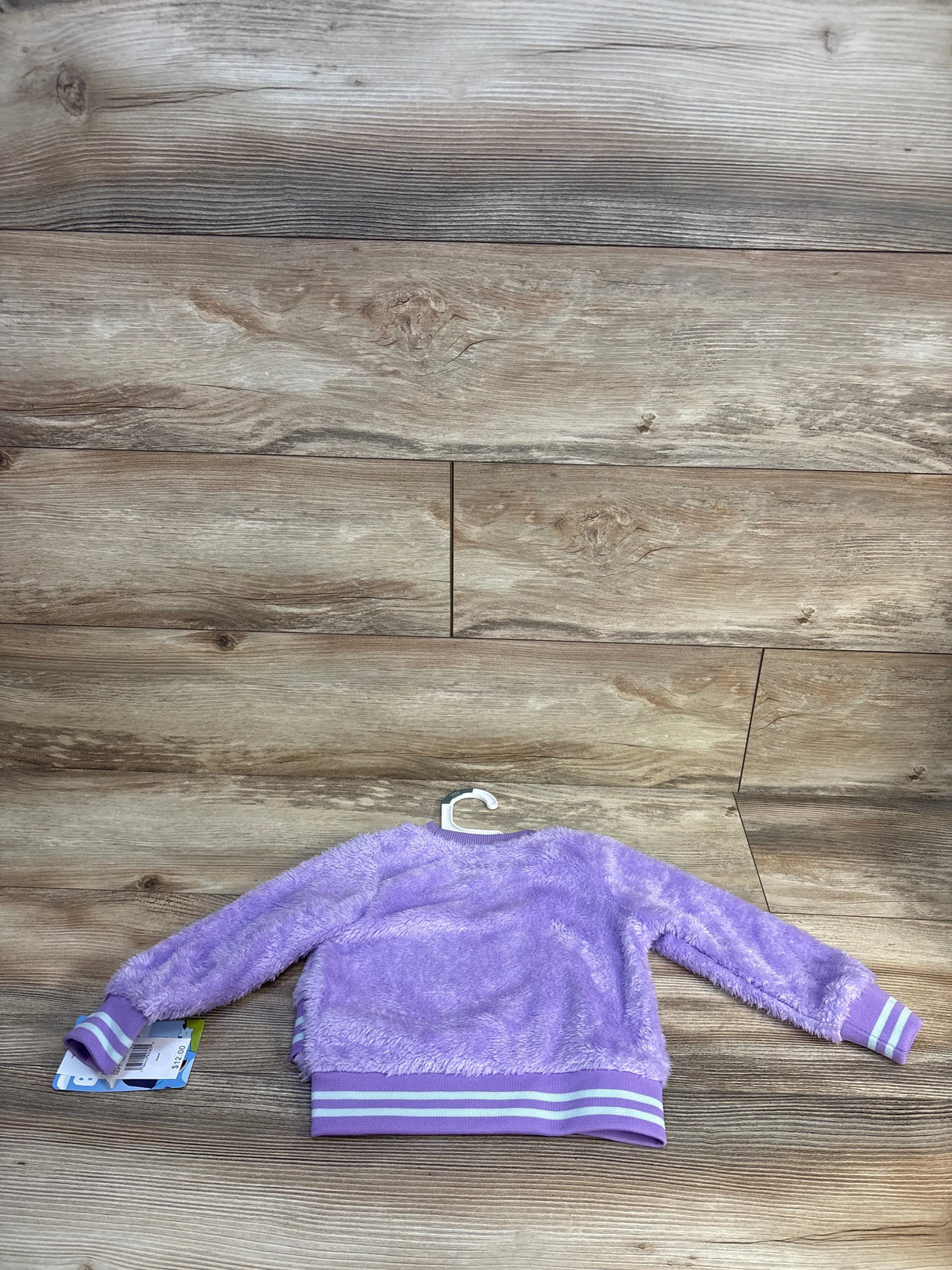 Purple fuzzy kids jacket with striped cuffs and hem, displayed on wooden background