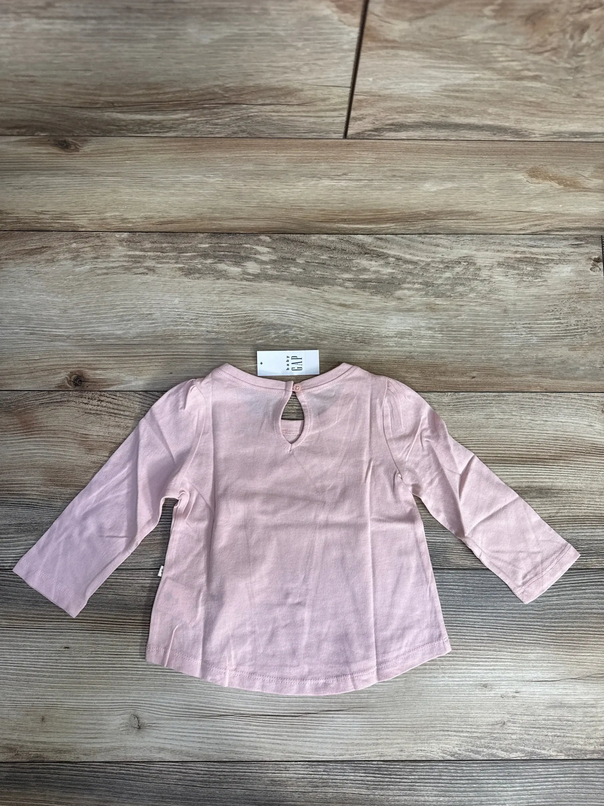 Light pink long sleeve baby shirt with back button detail on wooden floor