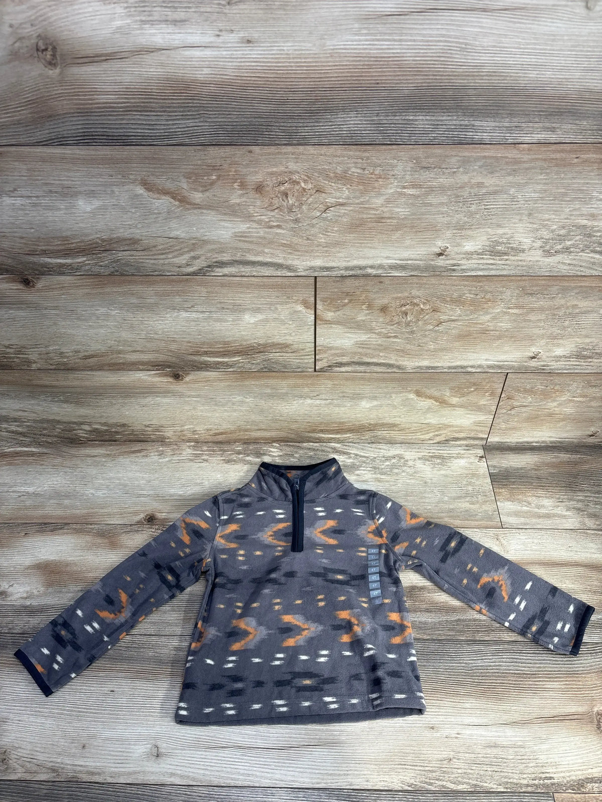 Kids fleece pullover with gray, orange, black geometric pattern and quarter zip on wooden floor