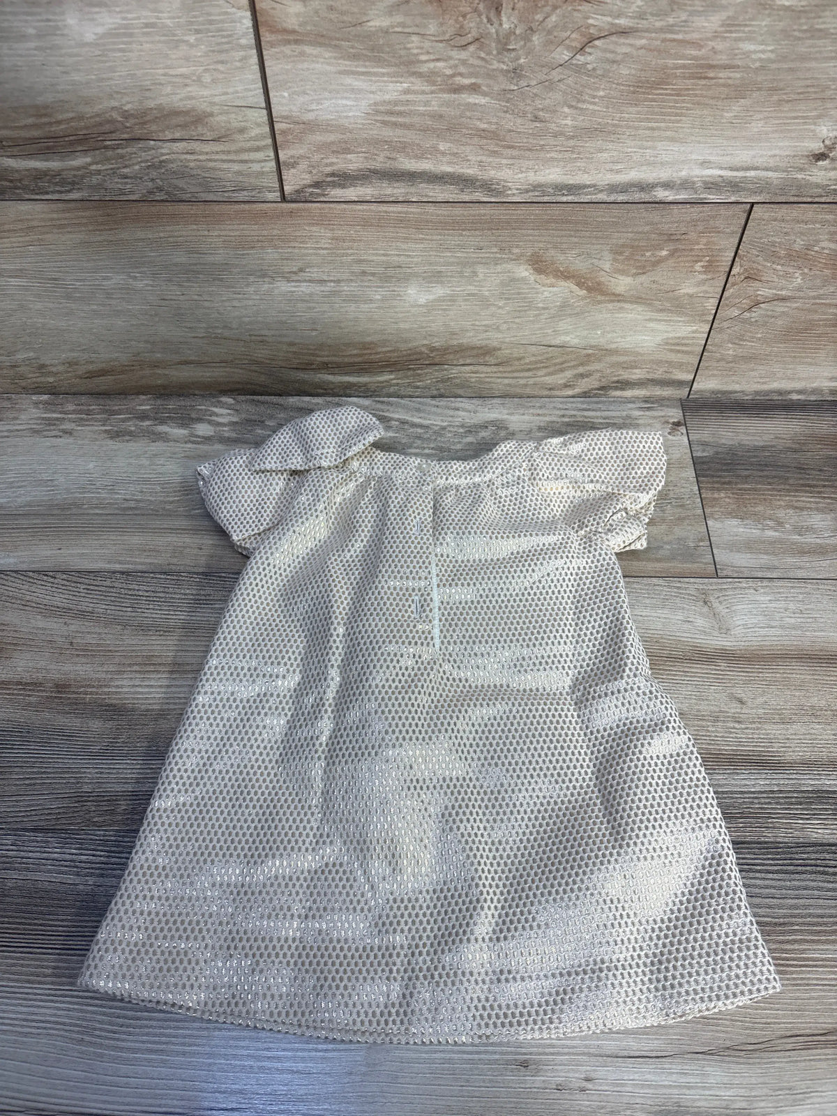 Back view of Janie & Jack gold metallic jacquard dress showing button closure and puff sleeves on wood floor