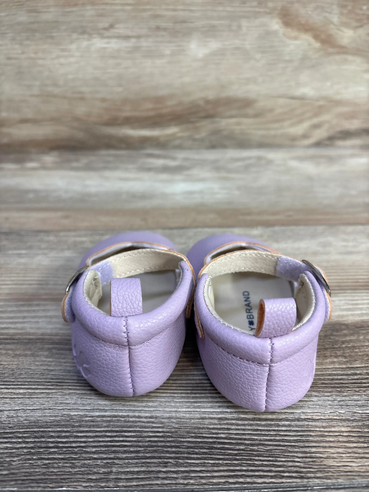 Rear view of Lucky Brand purple Mary Jane crib shoes size 3C showcasing pull tabs with a wood grain background