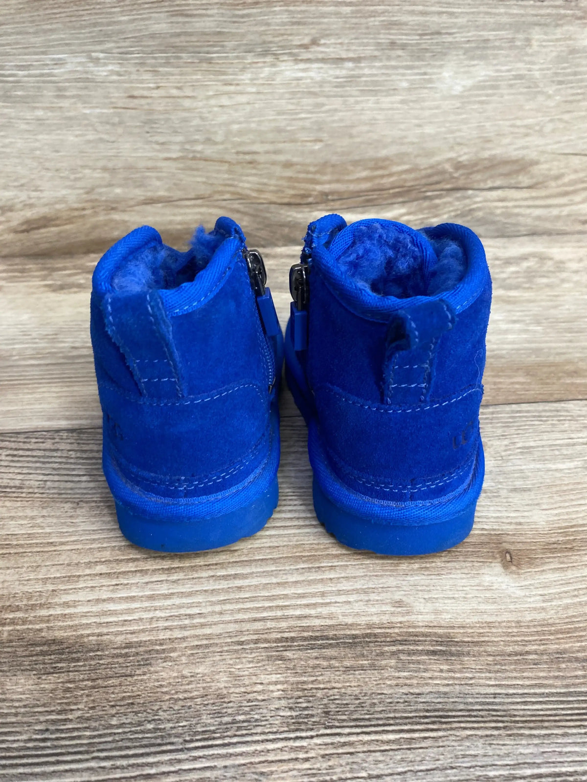 Back view of Ugg Neumel II boots in blue suede showcasing side zippers and fleece lining on wood plank floor