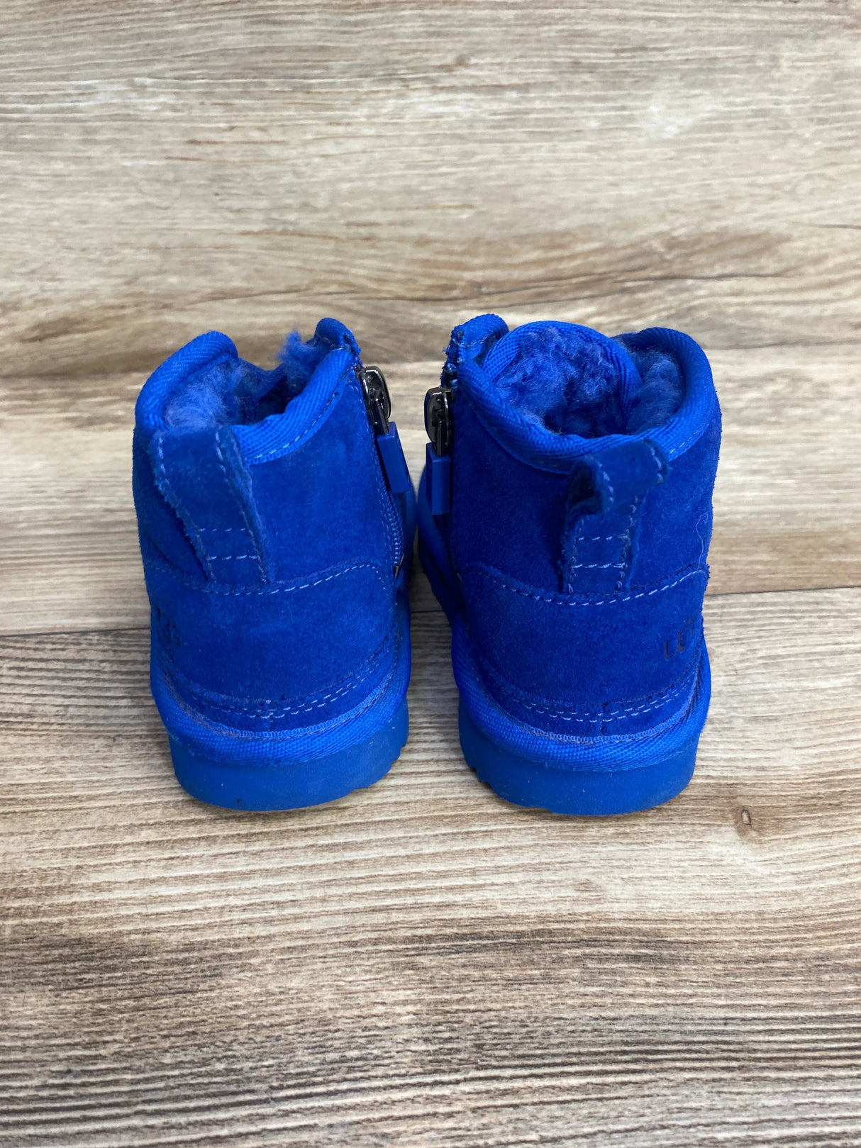 Back view of Ugg Neumel II boots in blue suede showcasing side zippers and fleece lining on wood plank floor