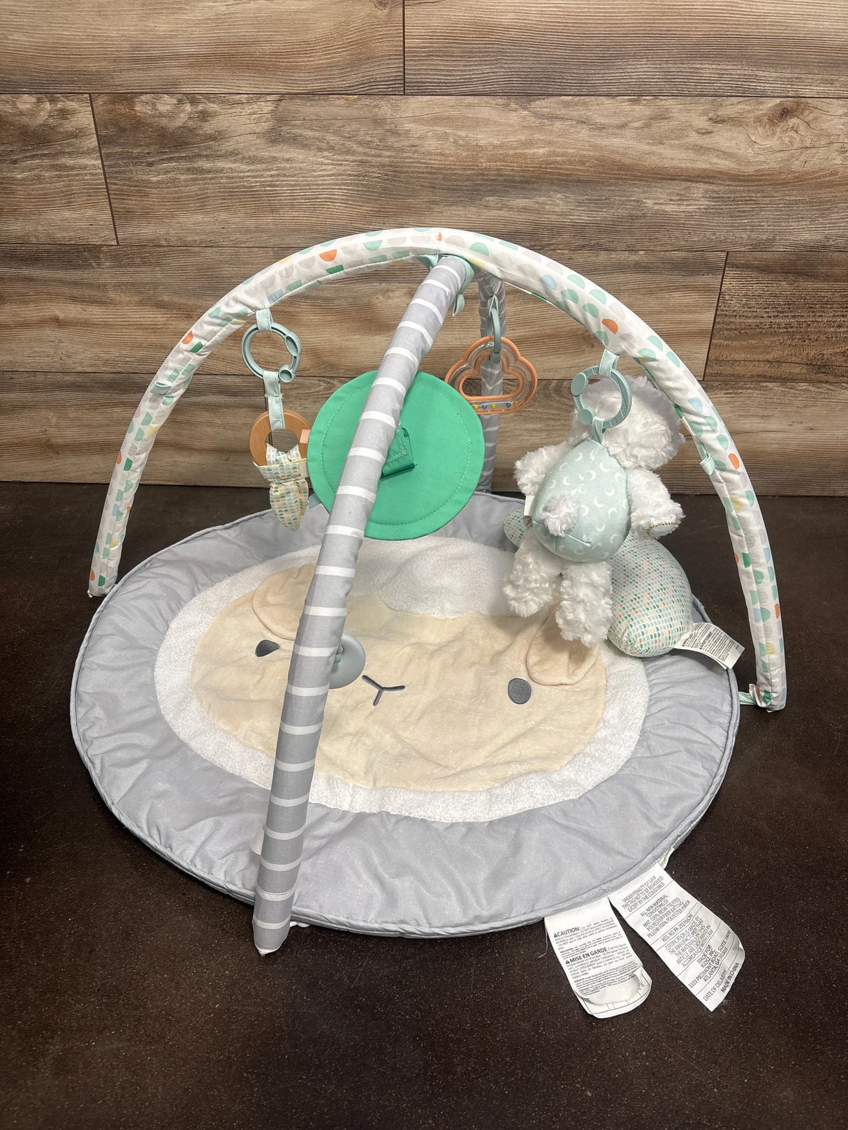 Top-down view of Sheppy’s Spot activity gym showing plush lamb mat and arched toy bars with hanging toys on wood backdrop