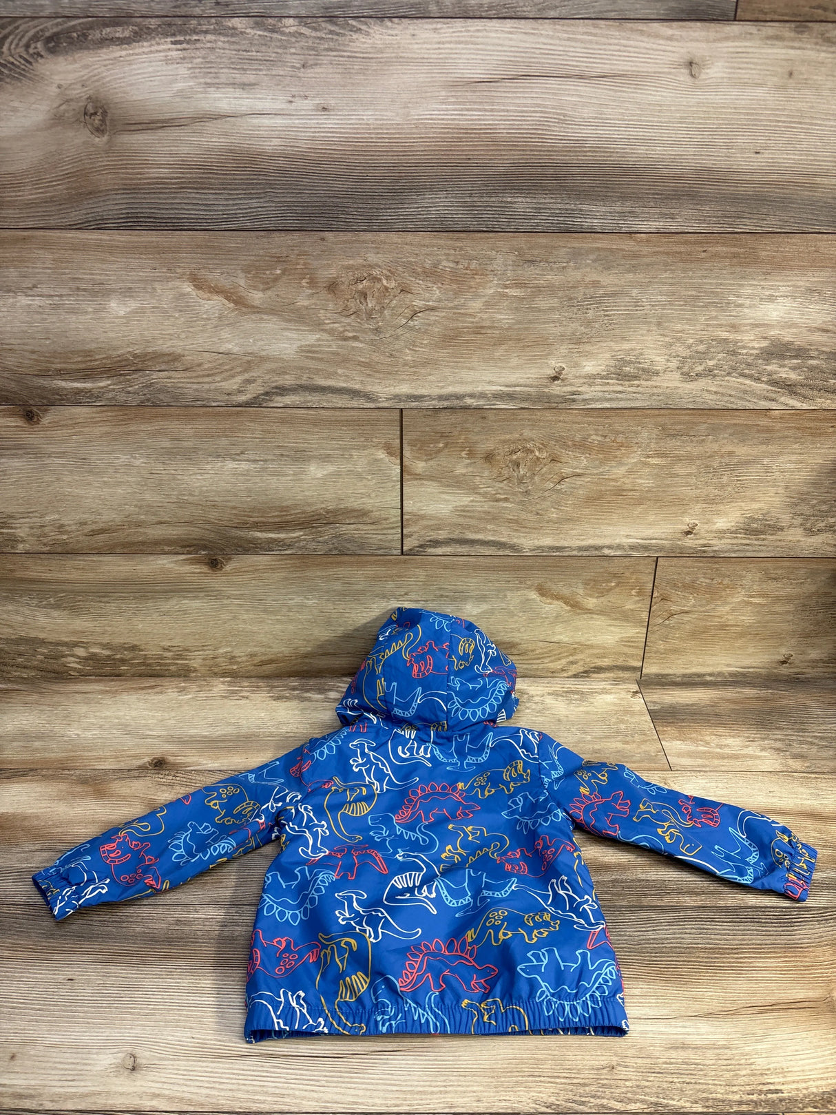 Back view of Cat and Jack toddler windbreaker jacket with blue multicolor dinosaur print and attached hood on wood background