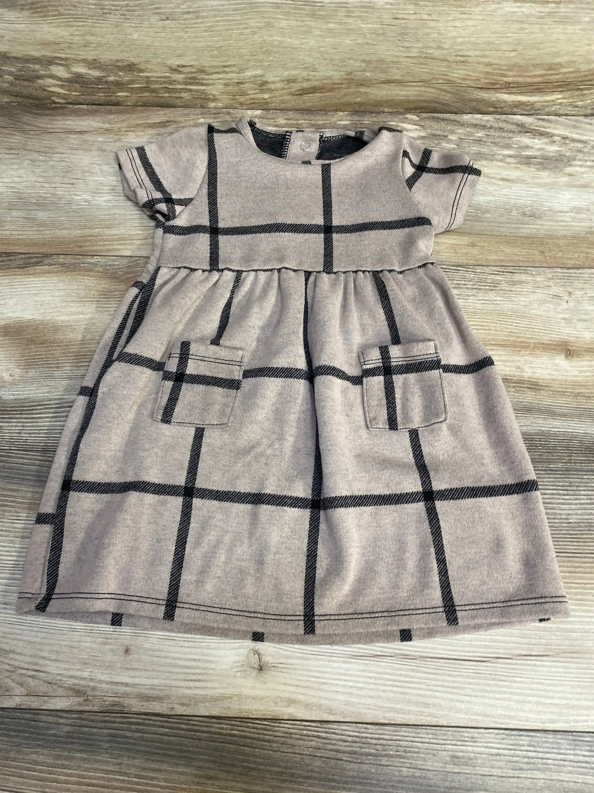 Flat lay of brown short-sleeve toddler dress showing windowpane check and patch pockets on wood background