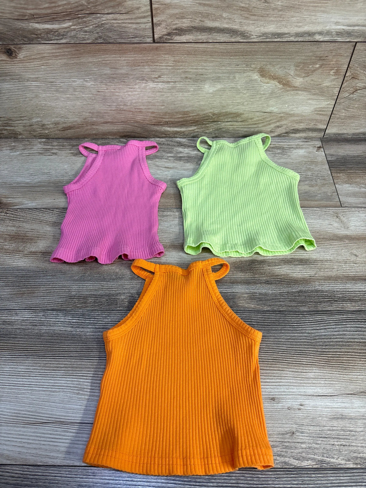 Front view of 3pk Ribbed Tank Tops sz 4T in pink, lime green, and orange showcasing scalloped hems on a wood-look floor