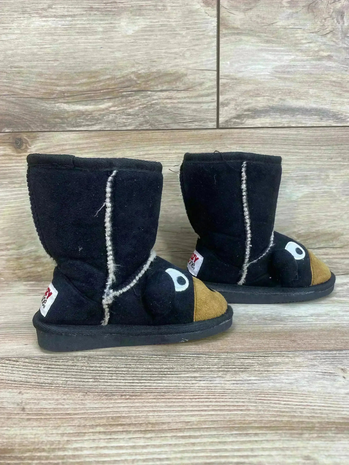 Side view of Lazy One kids moose slipper boots showing white contrast stitching and moose face details on wood floor