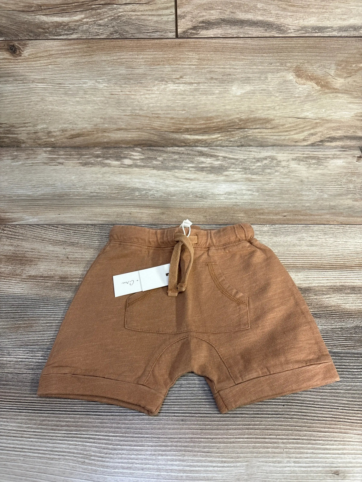 Front view of Rylee and Cru pouch shorts in caramel showcasing kangaroo pouch pocket and drawstring waist on wood plank background