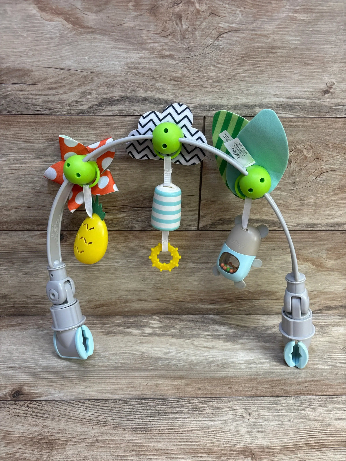 Front view of Taf Toys Tropical Orchestra Arch showcasing colorful hanging sensory toys and two clamps on a wood-grain background