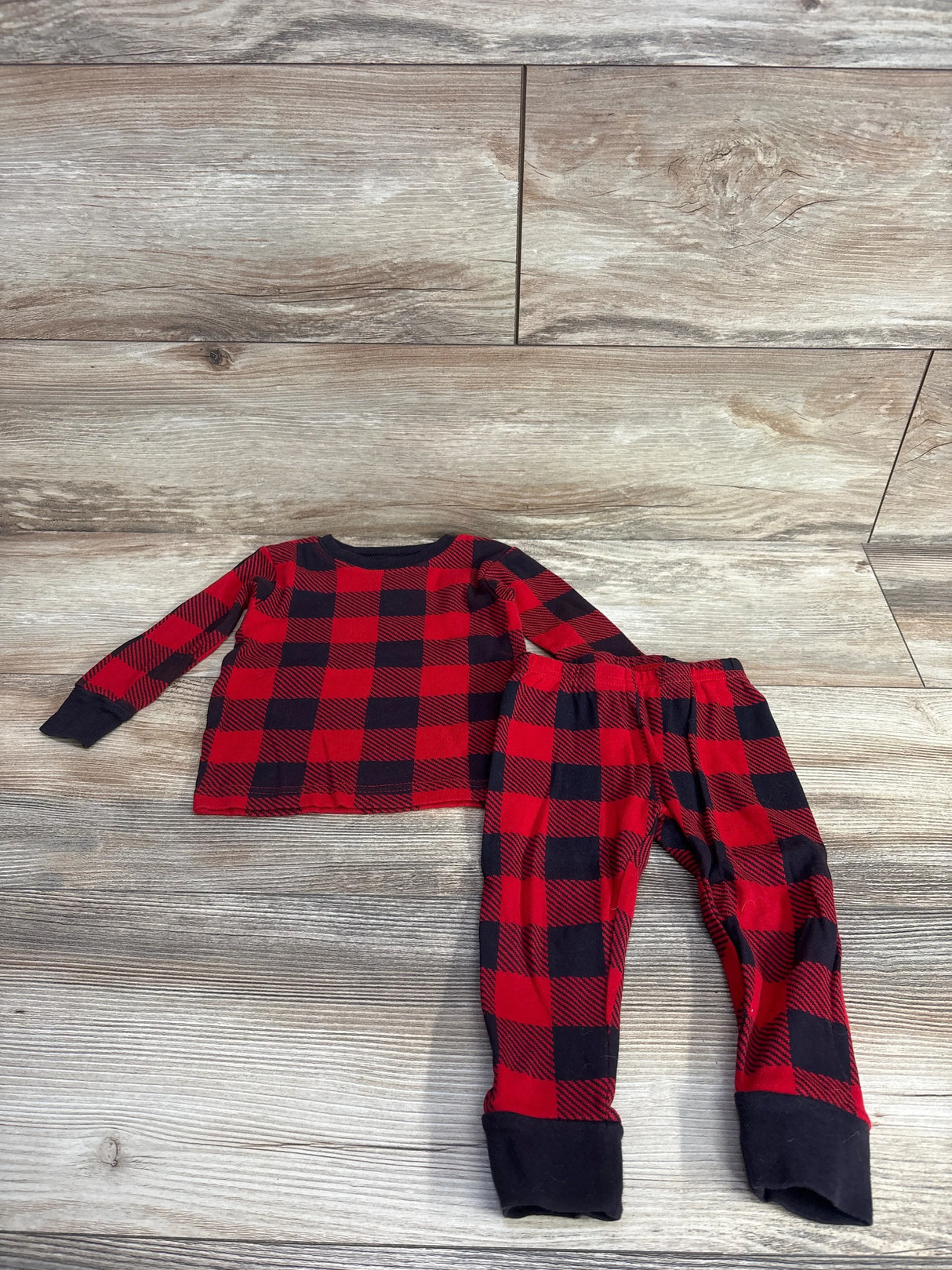 Red and black plaid kids pajama set with long sleeves and cuffed pants on wood floor