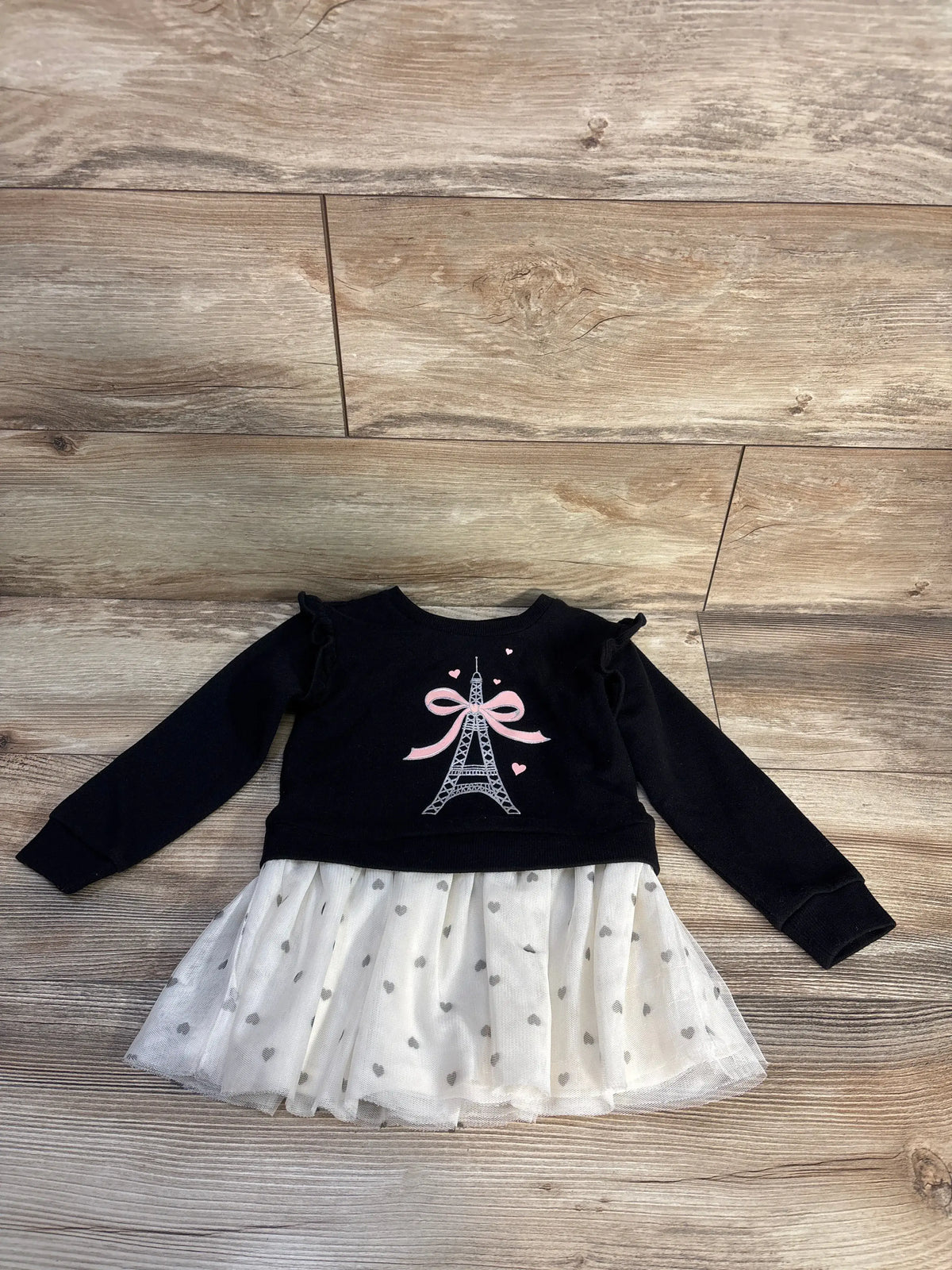 Front view of Children’s Place black sweatshirt dress showcasing glitter Eiffel Tower bow graphic and mesh skirt on wood floor