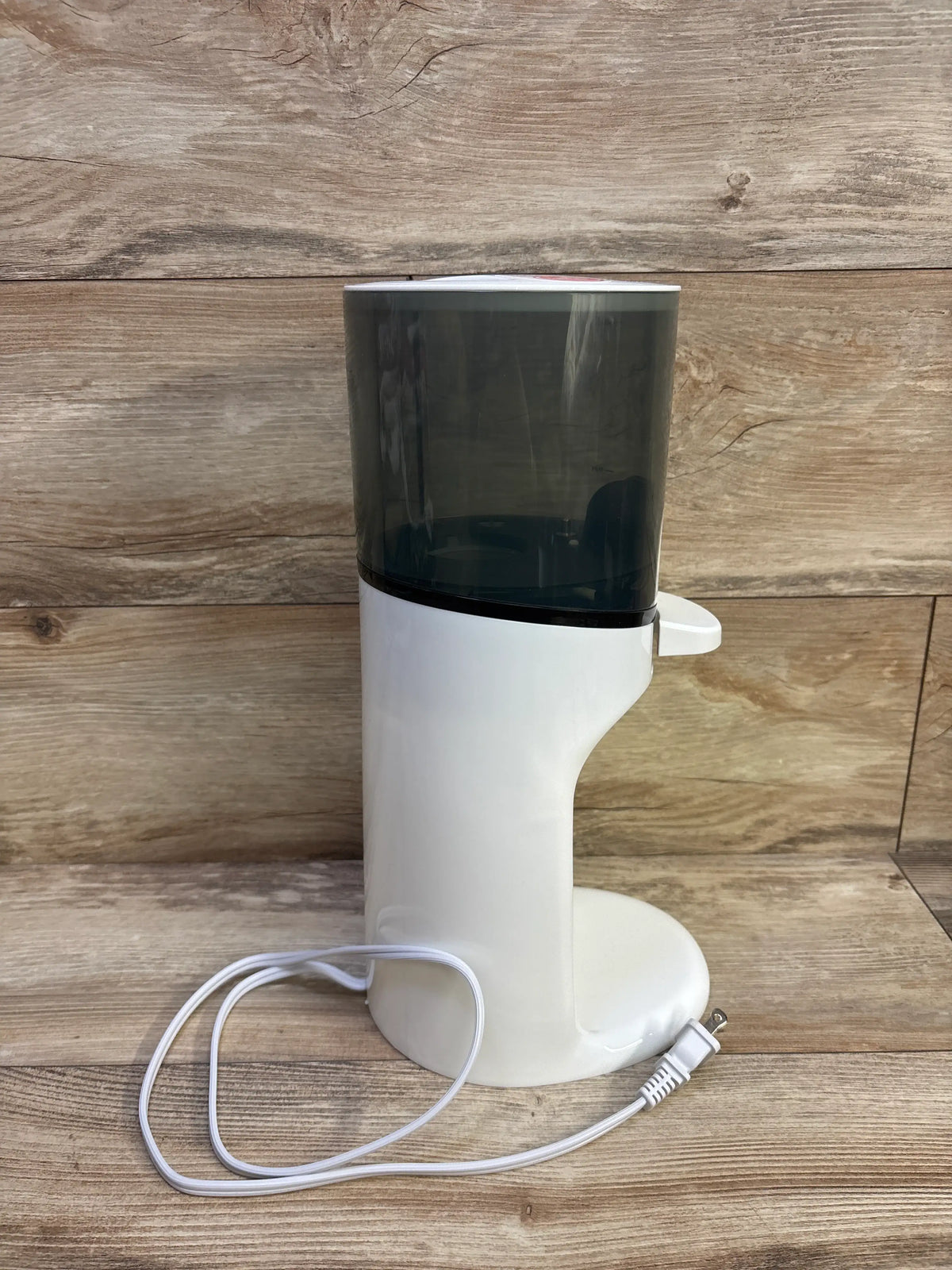 Front view of Baby Brezza Instant Bottle Warmer showcasing white housing, dark translucent upper chamber, and power cord on a wood surface