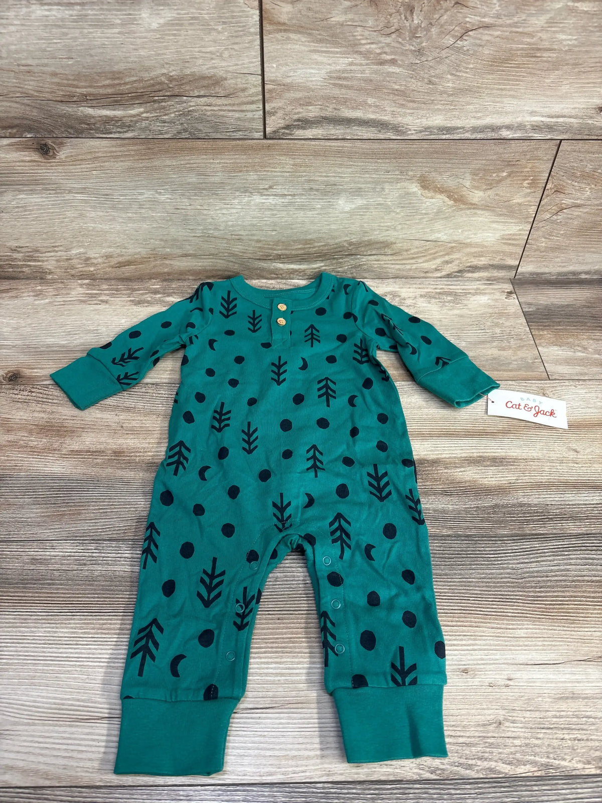 Teal baby romper with black tree and dot print, long sleeves, wooden buttons, laid flat on wood floor