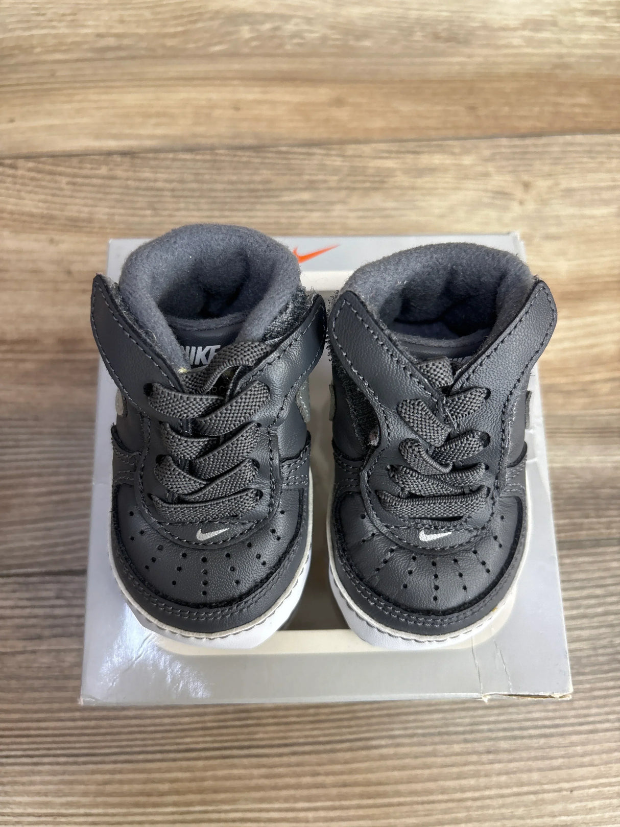 Black leather baby sneakers with laces on a box, toddler footwear on wood floor