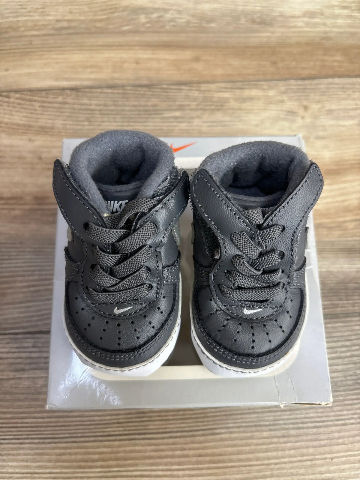 Black leather baby sneakers with laces on a box, toddler footwear on wood floor