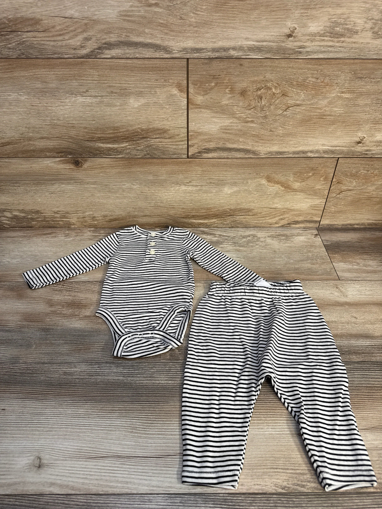 Black and white striped long sleeve baby bodysuit and matching pants on wooden floor