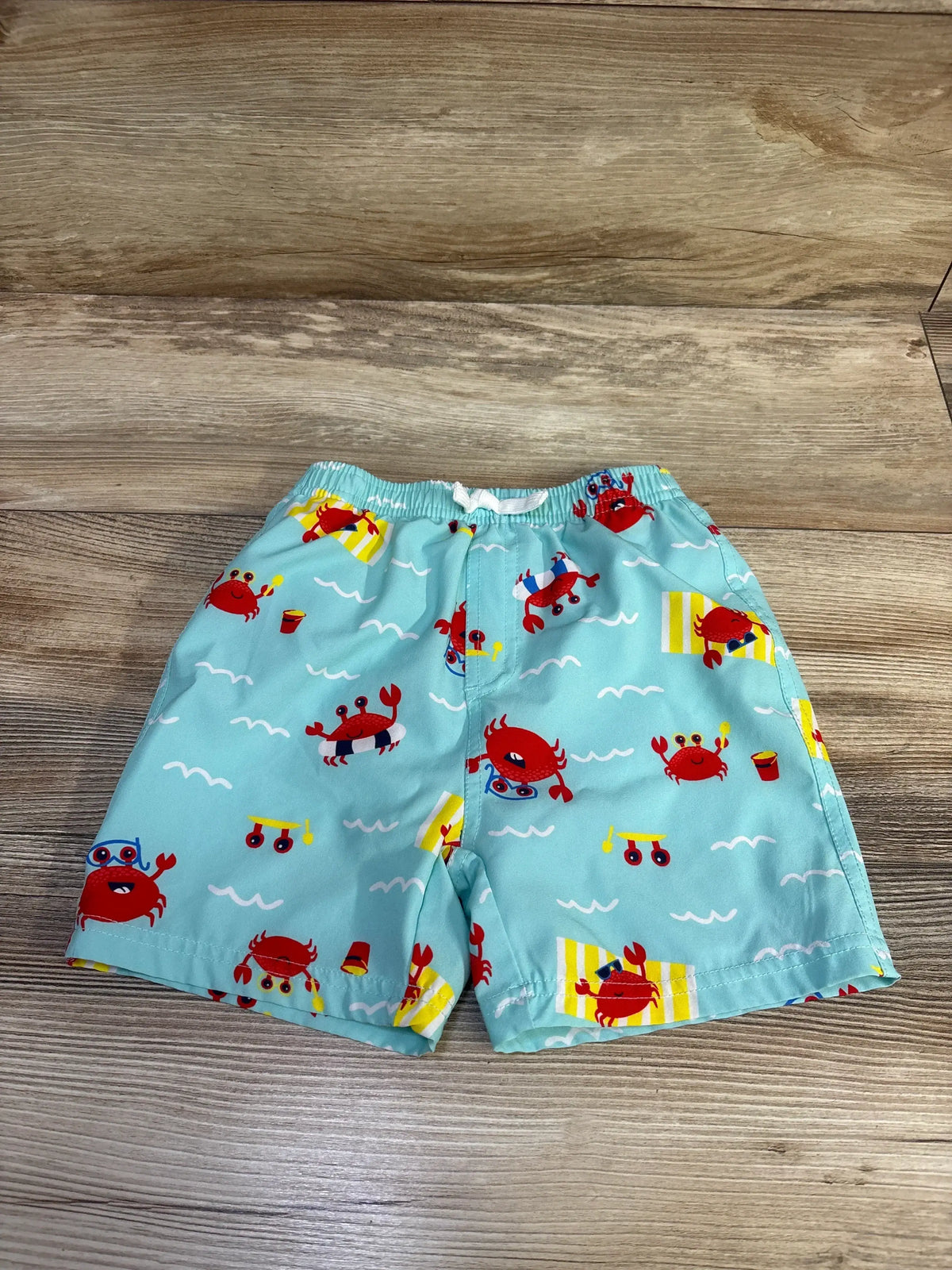 Front view of Banana Boat swim trunks in seafoam showcasing crab print and elastic waist with wood-grain background