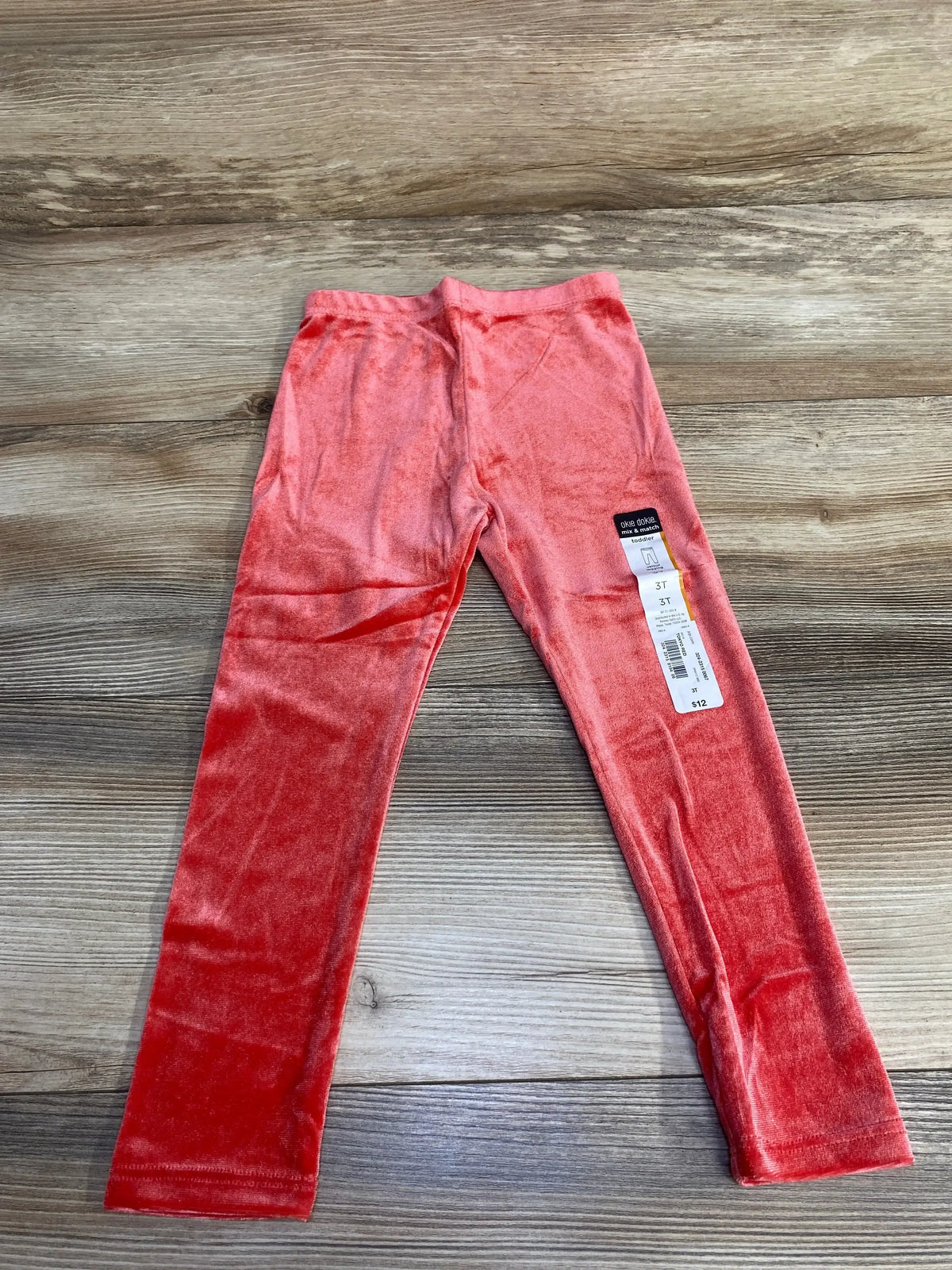 Top-down view of red velour toddler leggings size 3T showcasing plush fabric and elastic waist on wood background