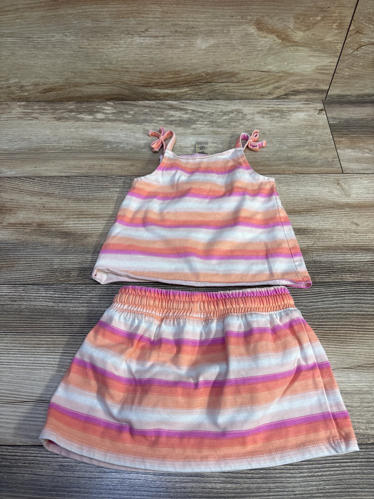 Flat lay of peach striped 2-piece tank top and skort showing tie shoulder straps and elastic waistband on wood background