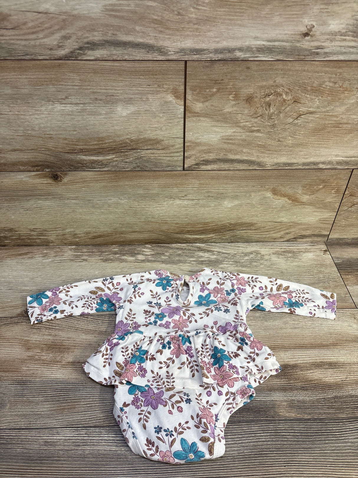 Flat lay of Carter’s ivory floral long-sleeve skirted bodysuit showcasing ruffled peplum on wood floor background