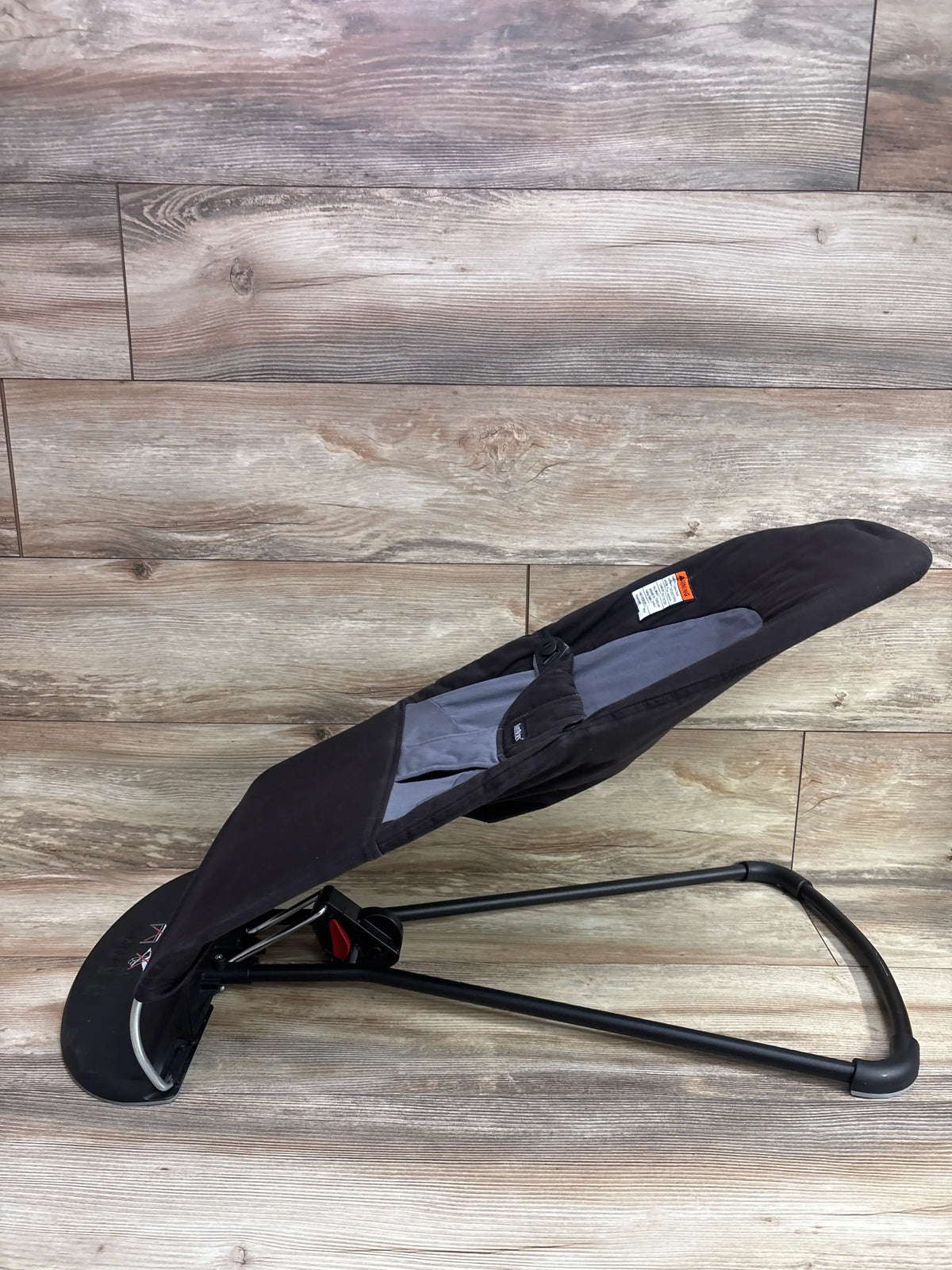 Angled view of BabyBjörn Balance Soft Bouncer in Black/Dark Grey with reclining seat, harness, and black frame on a wood-look floor