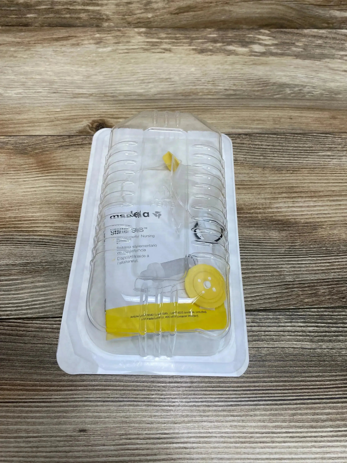 Top-down view of Medela Starter Supplemental Nursing Tubing (SNS) in clear blister pack showing sterile tubing and yellow connectors on wood tabletop