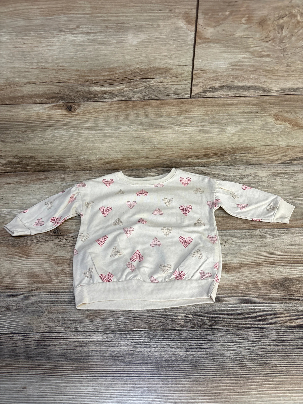 Cream long sleeve baby sweatshirt with pink and beige heart print on wood floor