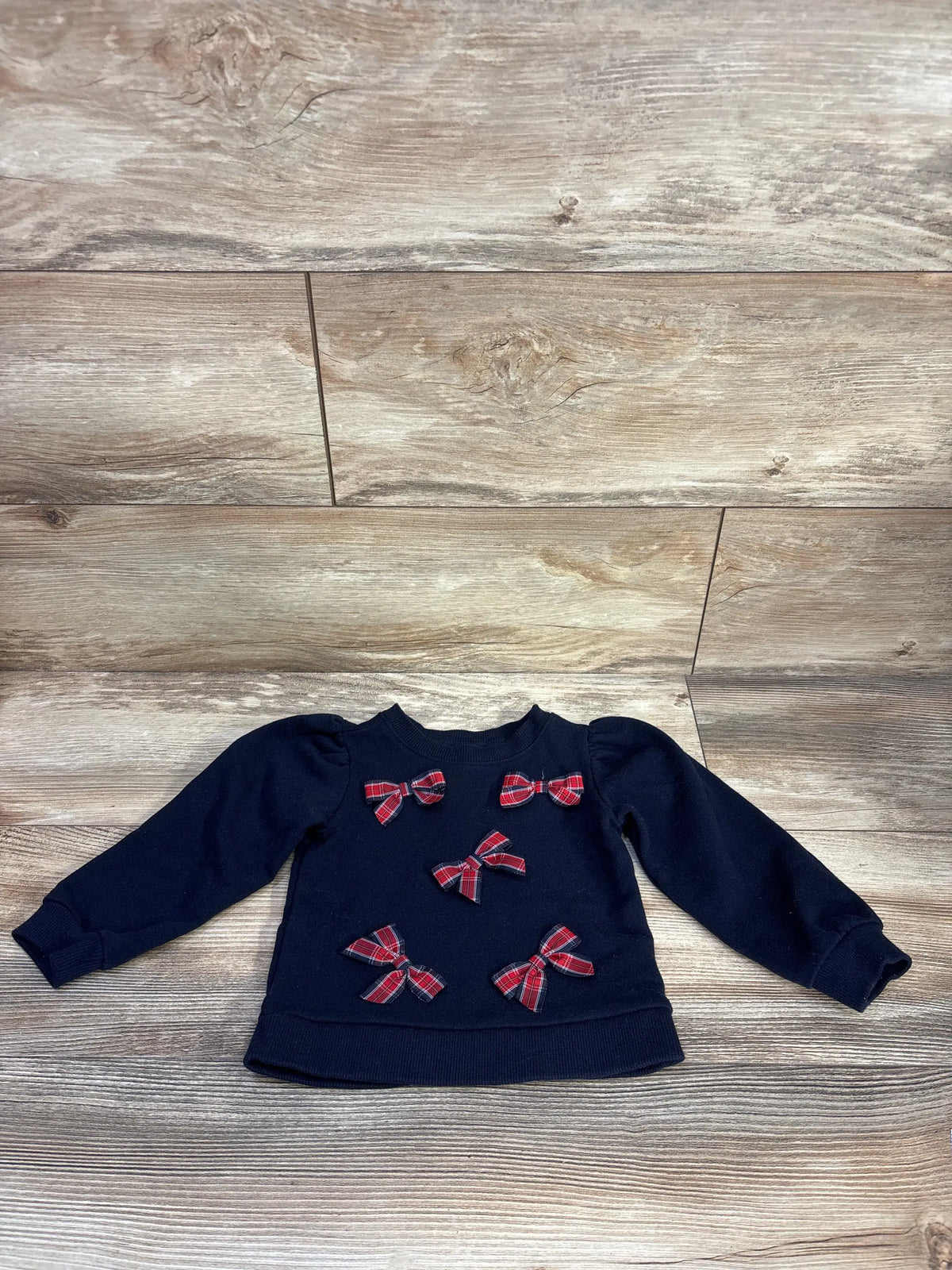 Front view of Janie & Jack 2T tartan bow sweatshirt showing five bows, ribbed trim, and navy fabric on wood flooring
