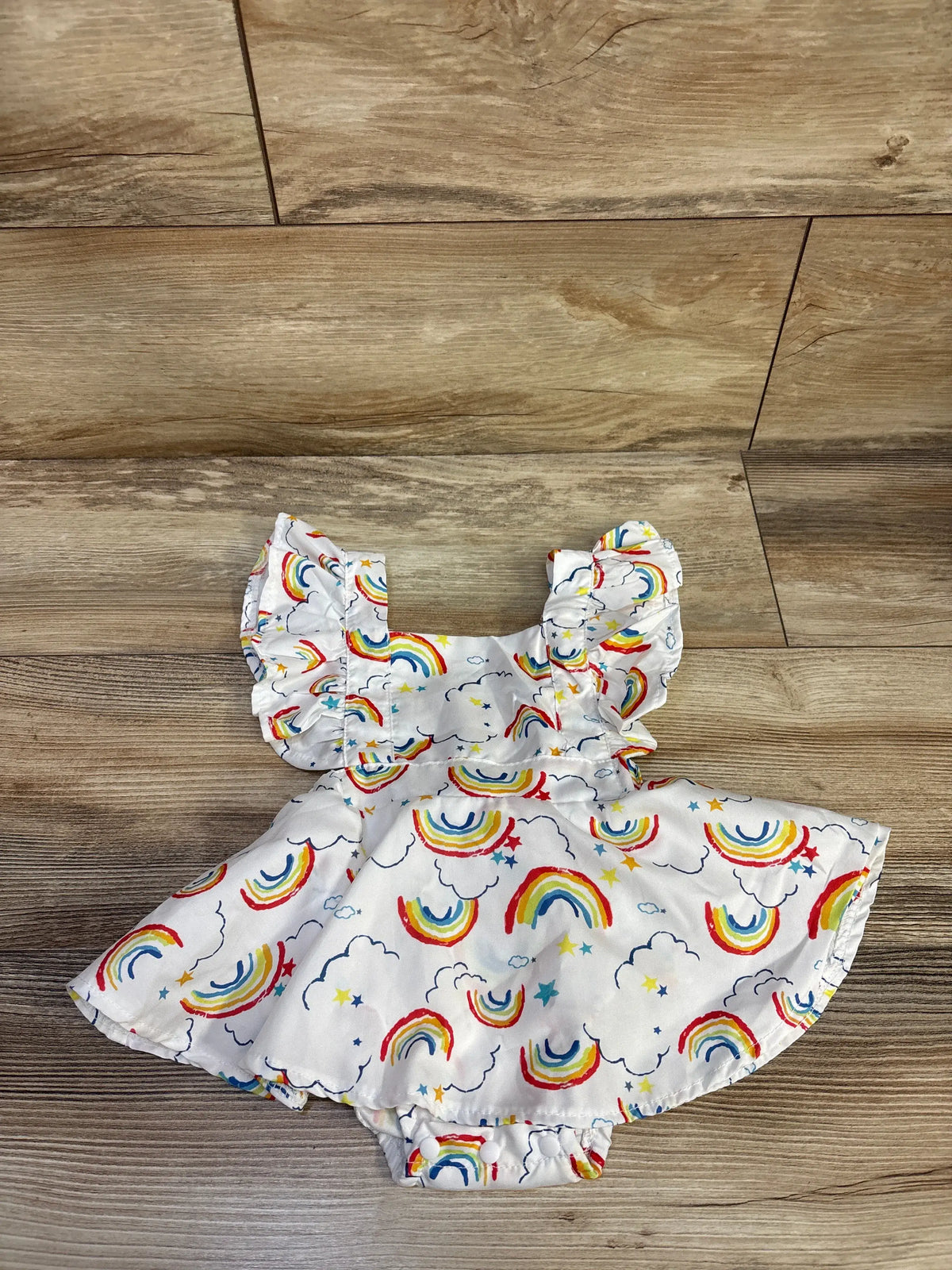 Top view of white rainbow print bodysuit dress showcasing puff sleeves and diaper-cover bottom on a wood-look floor