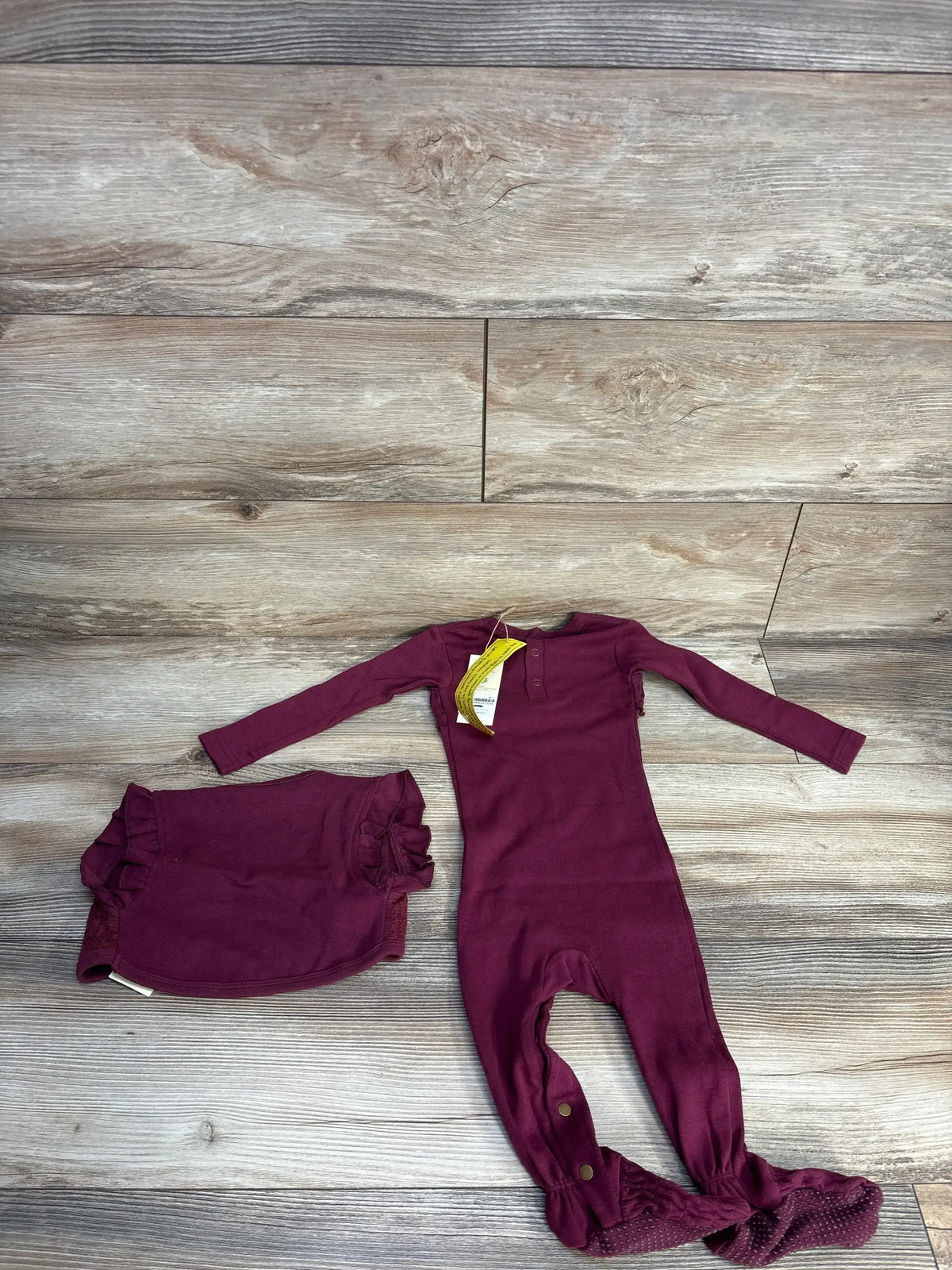 Flat lay of L'oved Baby smocked footie with built-in footies and matching ruffle diaper cover in cranberry on wood floor