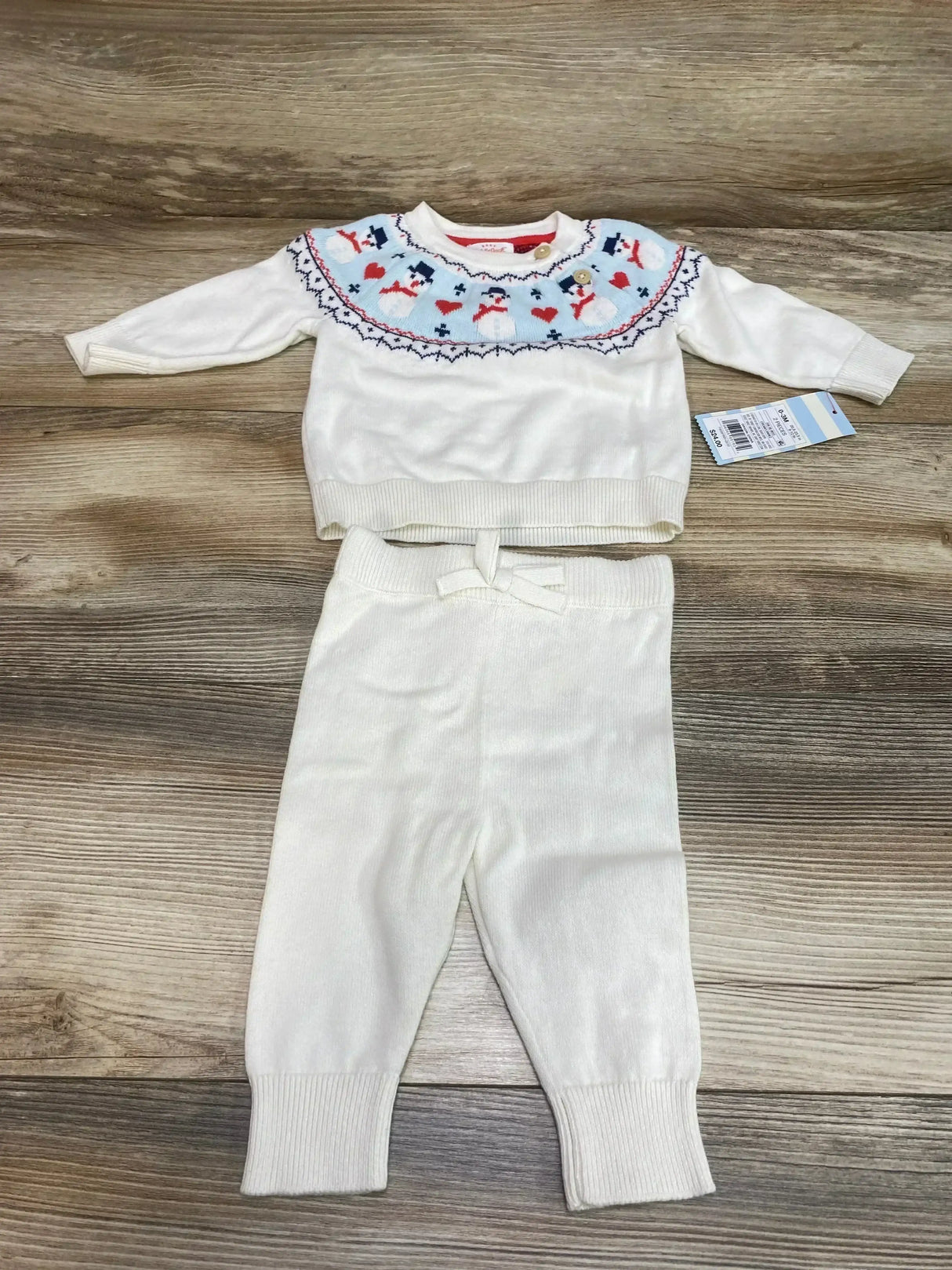 Front view of white baby sweater and pants set (0–3 months) with fair isle snowman yoke, laid flat on wood background
